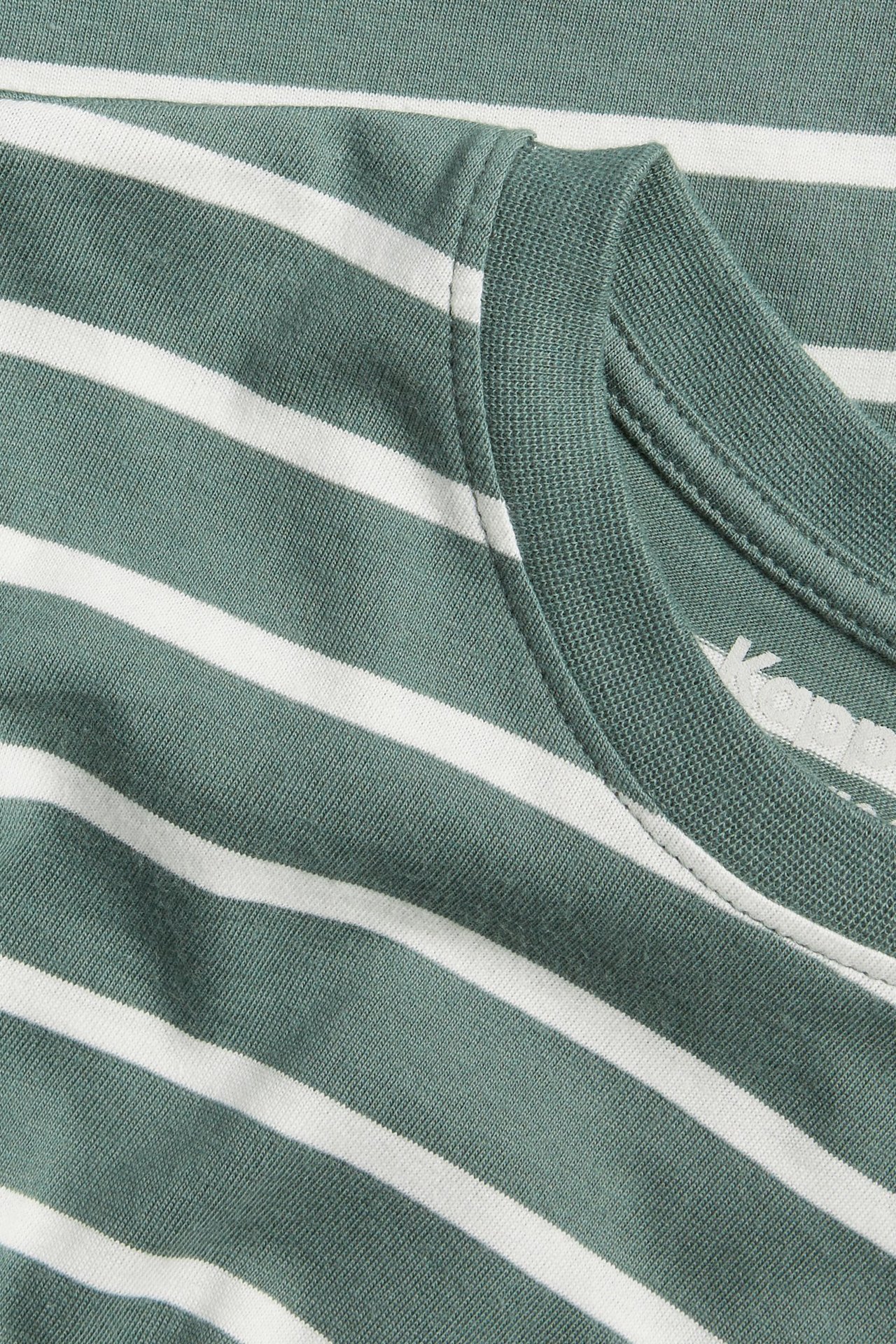 Zbliżenie na ciemnozielono-białą bawełnianą koszulkę z długim rękawem w paski, z prążkowanym dekoltem.