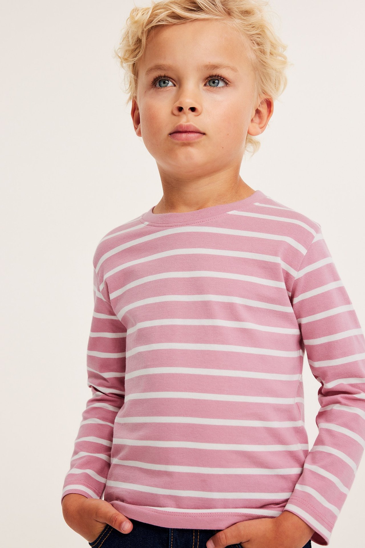 Edestä, lapsi vaaleanpunaisessa ja valkoraidallisessa pitkähihaisessa puuvilla-t-paidassa ja tummansinisissä farkuissa.