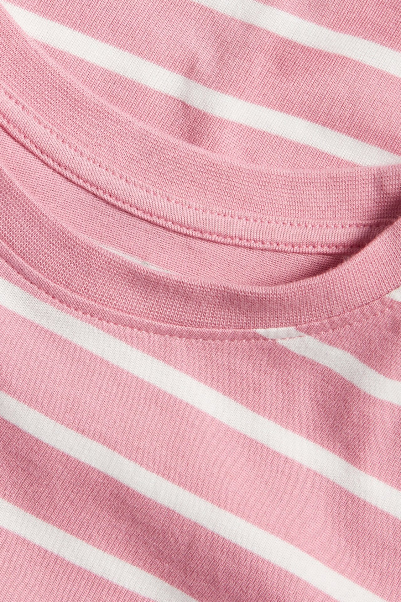 Zbliżenie na różowo-białą, pasiastą, bawełnianą koszulkę z długim rękawem i prążkowanym dekoltem.