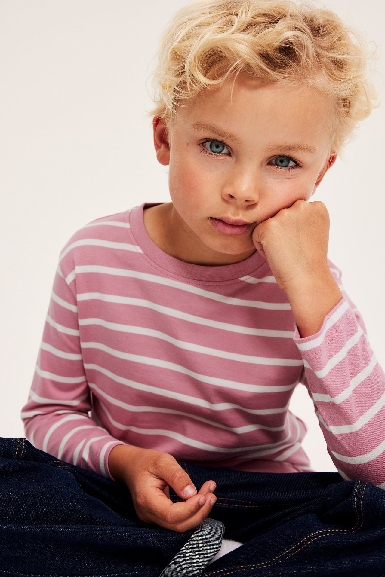 Edestä kuvattu lapsi yllään vaaleanpunainen-valkoraidallinen pitkähihainen puuvillapaita ja tummansiniset farkut.