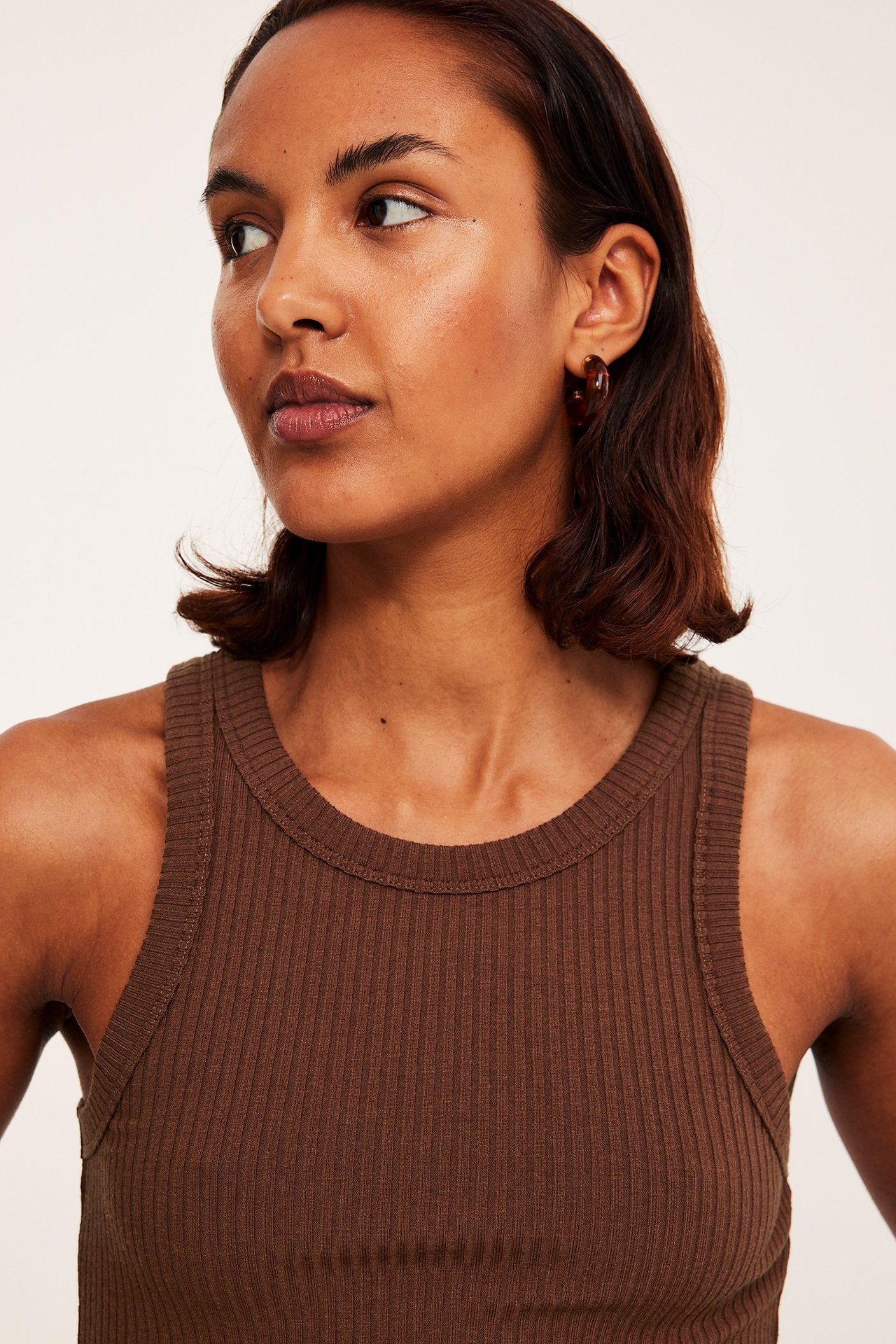 Nærbilde forfra av en kvinne i en brun ribbet singlet og brune ringøreringer.