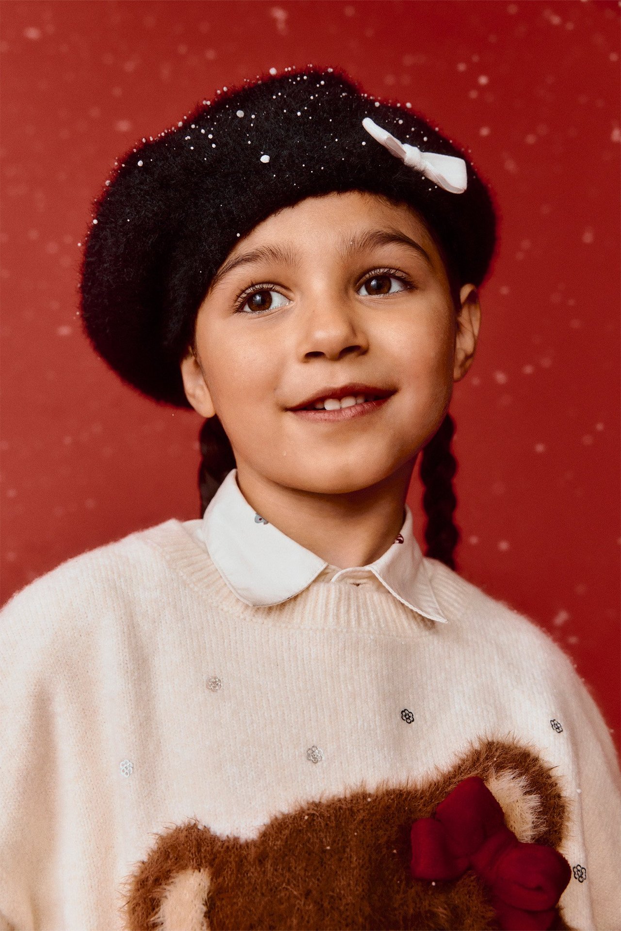 Zbliżenie dziecka w czarnym dzianinowym berecie z białą kokardą, na beżowym swetrze i białej koszuli.