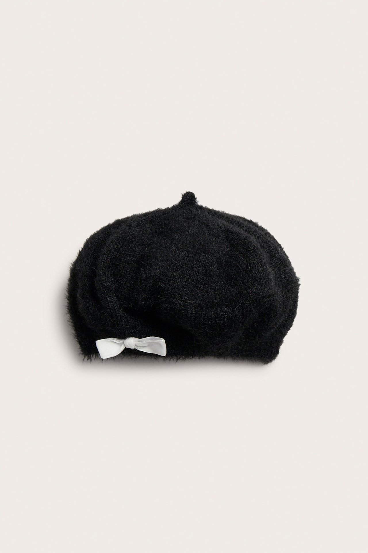 Widok z przodu czarnego dzianinowego beretu z czesanego poliestru z małą białą aksamitną kokardą.