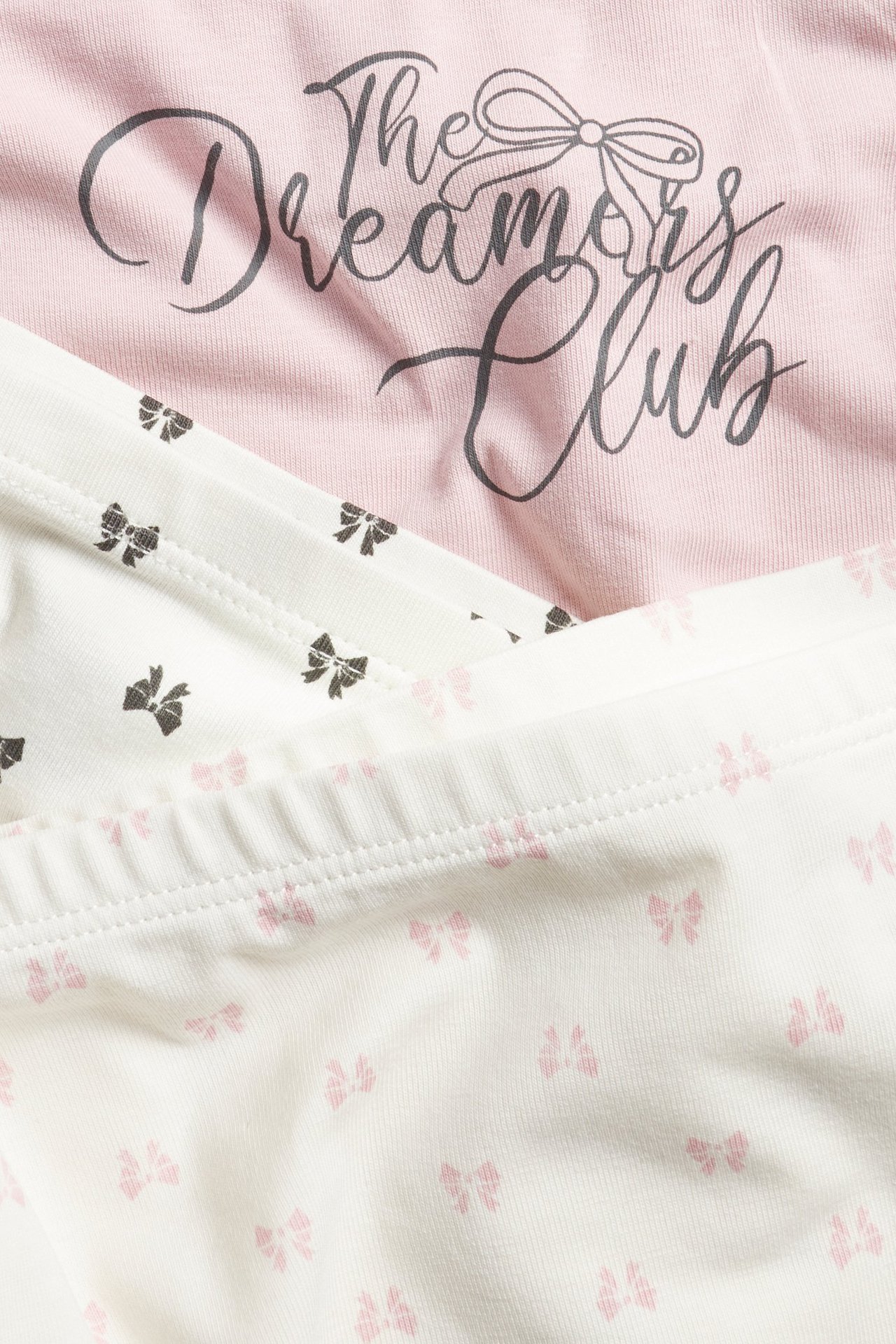 Lähikuva kolmista lasten bokserialushousuista: vaaleanpunaiset tekstillä, kahdet luonnonvalkoiset rusettikuvioilla.