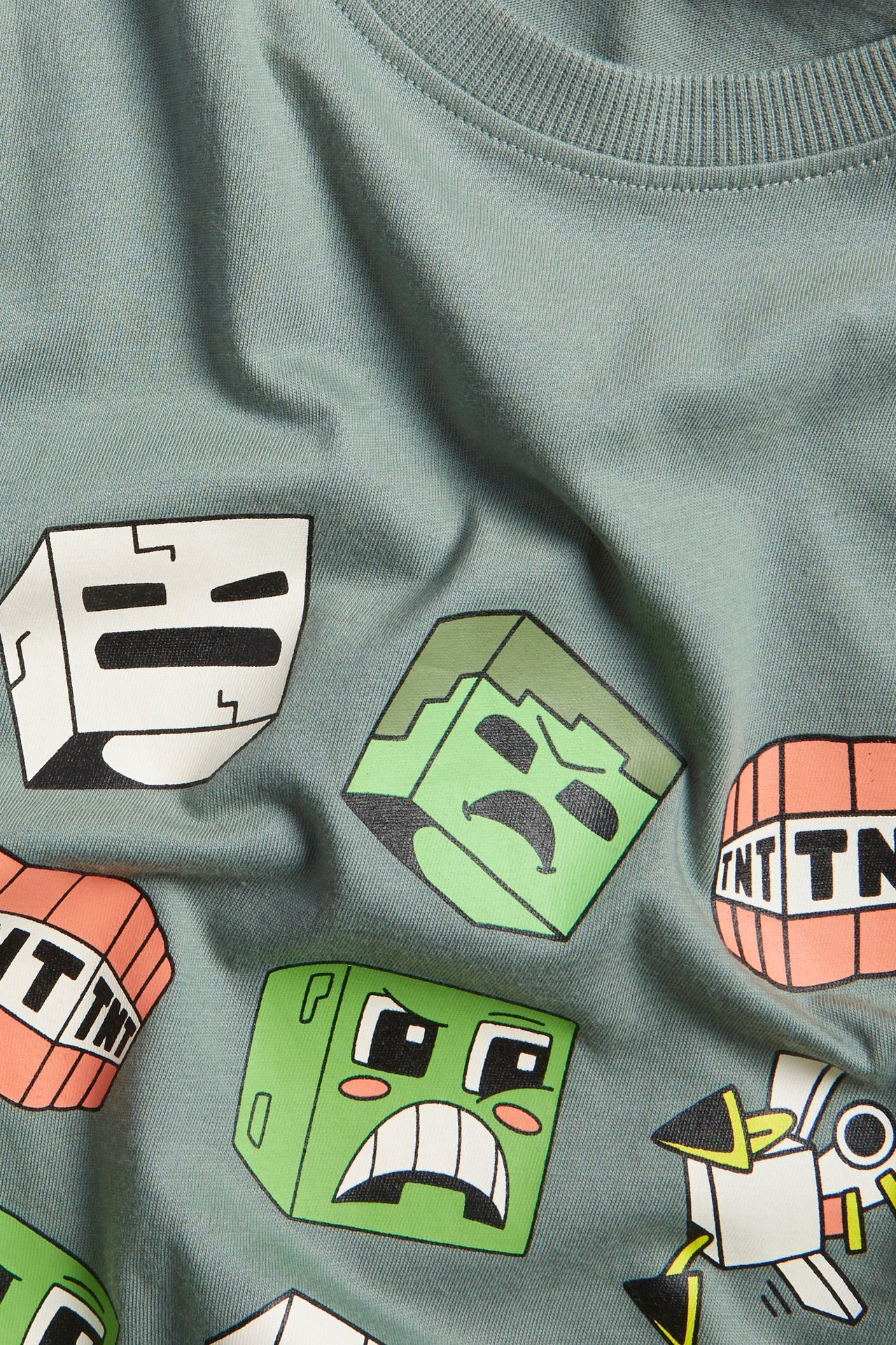 Närbild på en ljusgrön t-shirt i bomull för barn med ribbad halsringning och färgglatt Minecraft-tryck.