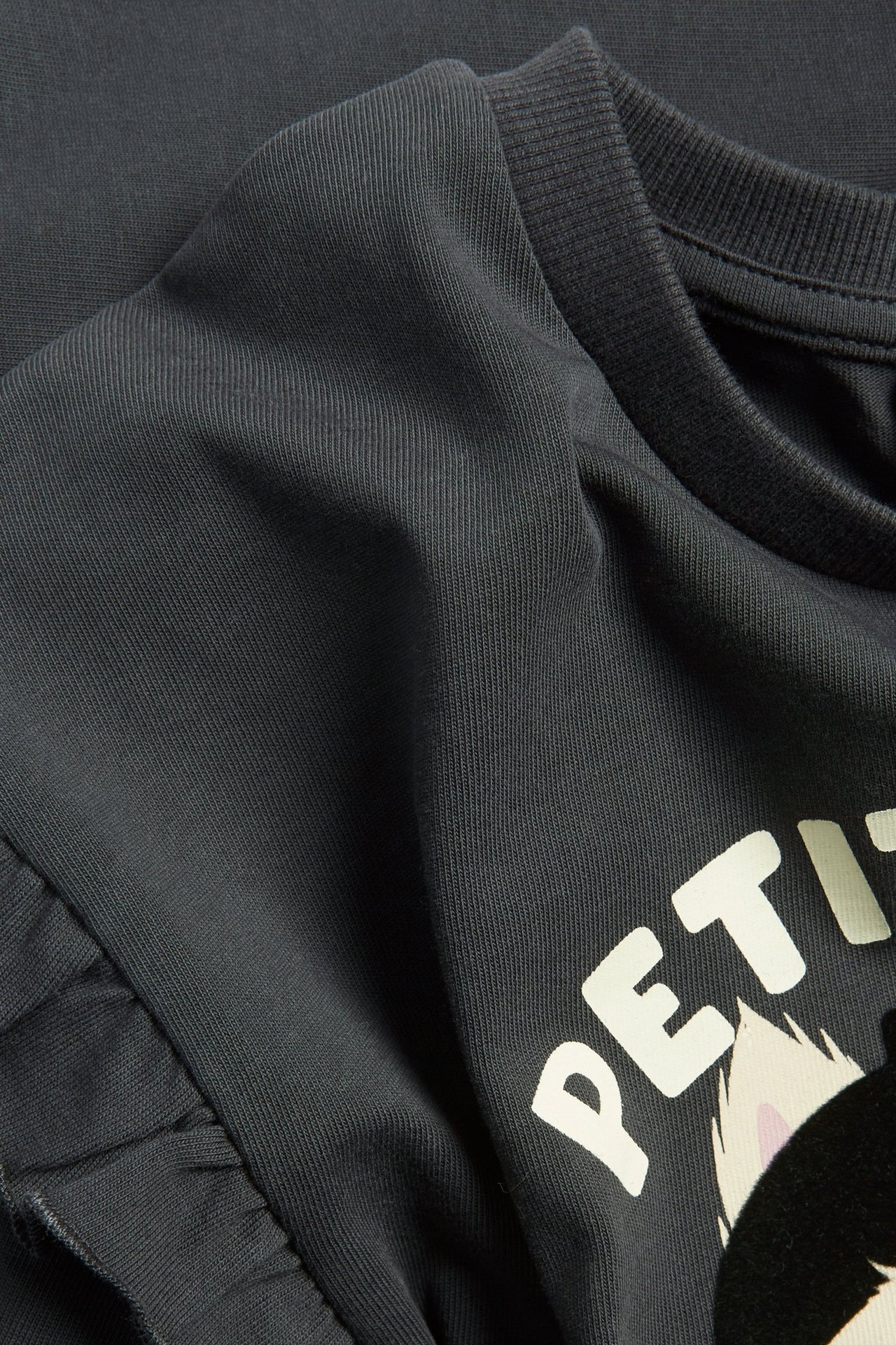 Zbliżenie na ciemnoszarą bawełnianą bluzę z białym nadrukiem kota i falbanką na rękawie.