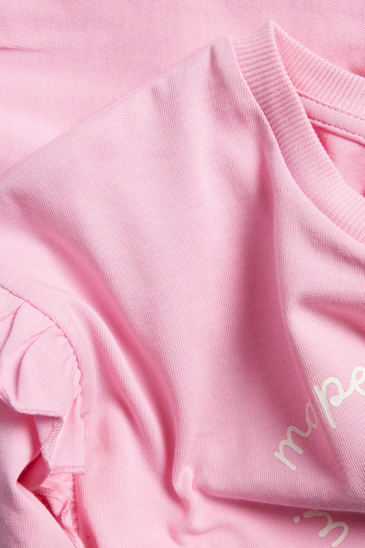 Zbliżenie jasnoróżowej bawełnianej bluzy z nadrukiem z przodu i falbanką na rękawie.