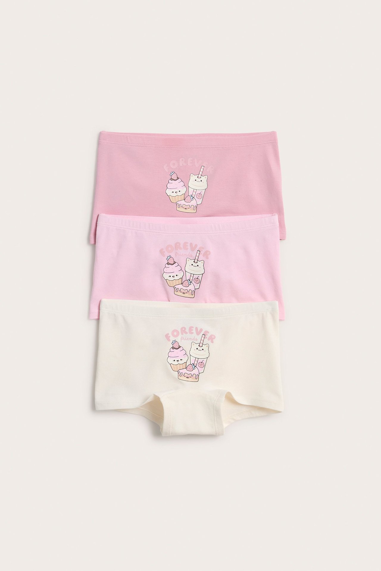 Widok z przodu trzech bokserek dziecięcych: dwie różowe i jedna jasnobeżowa, wszystkie z nadrukiem.