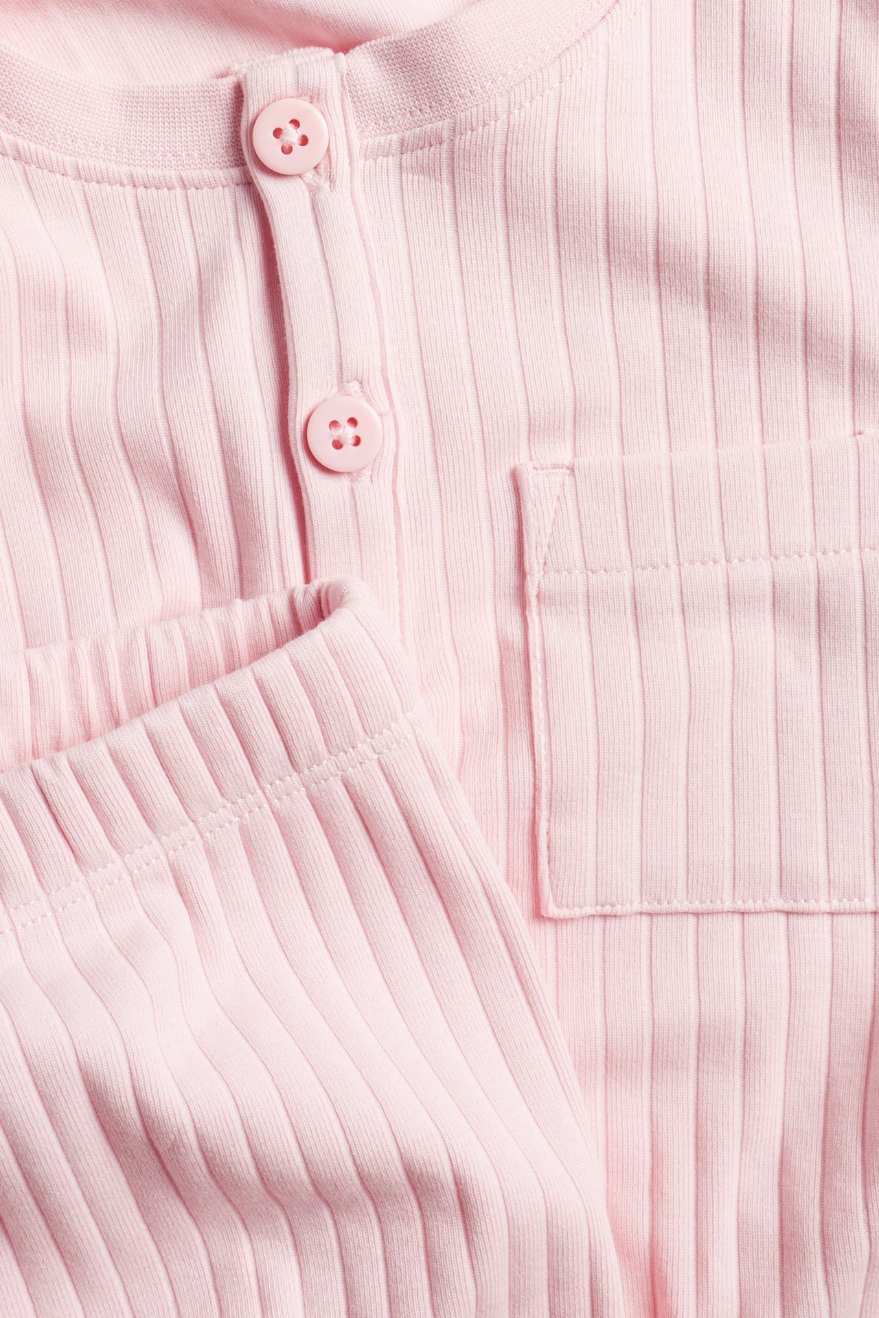 Zbliżenie różowej prążkowanej piżamy z długim rękawem, z listwą guzikową i kieszenią, z pasującymi spodniami.