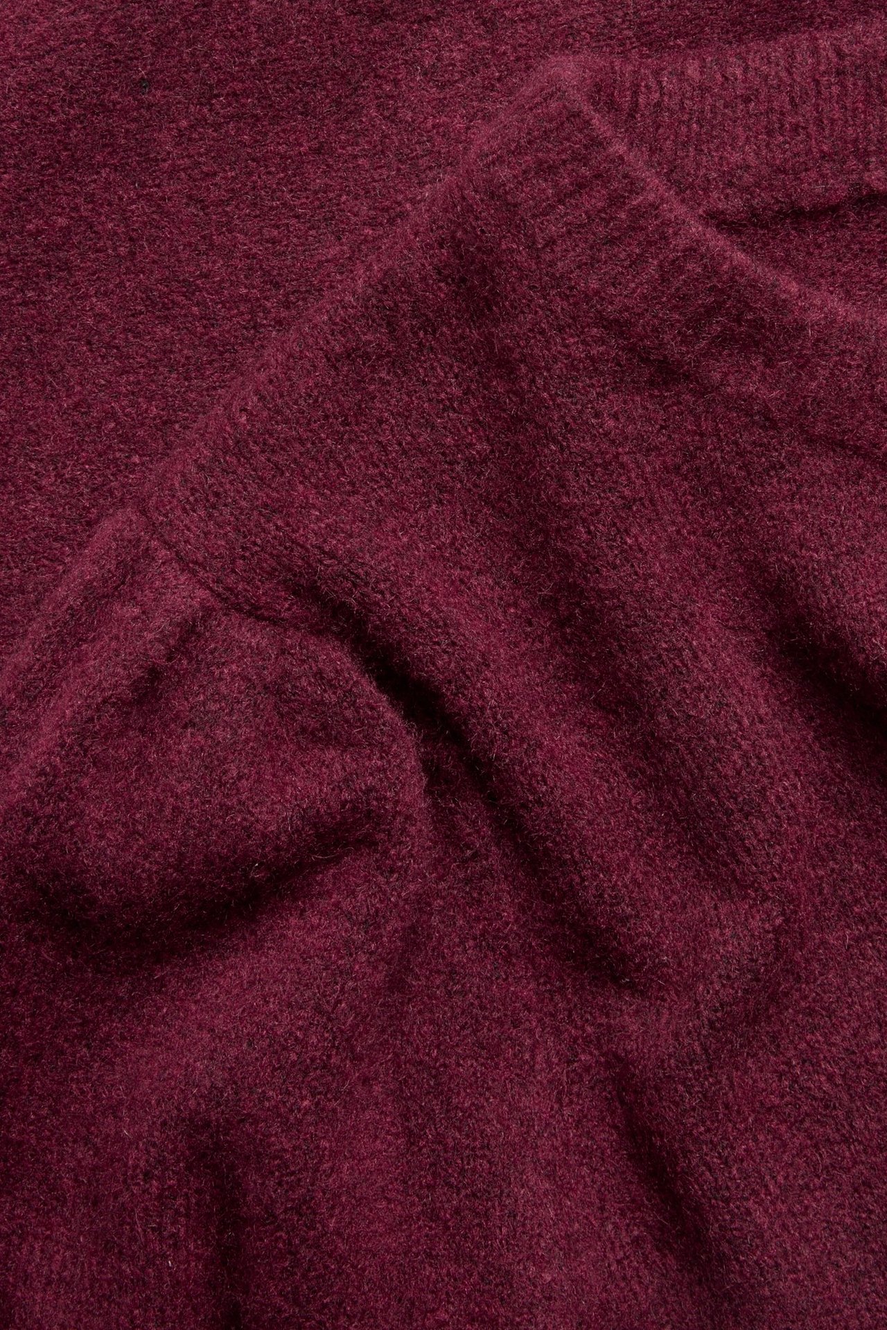 Zbliżenie na bordowy melanżowy dzianinowy T-shirt z widocznym detalem bufiastych rękawów.