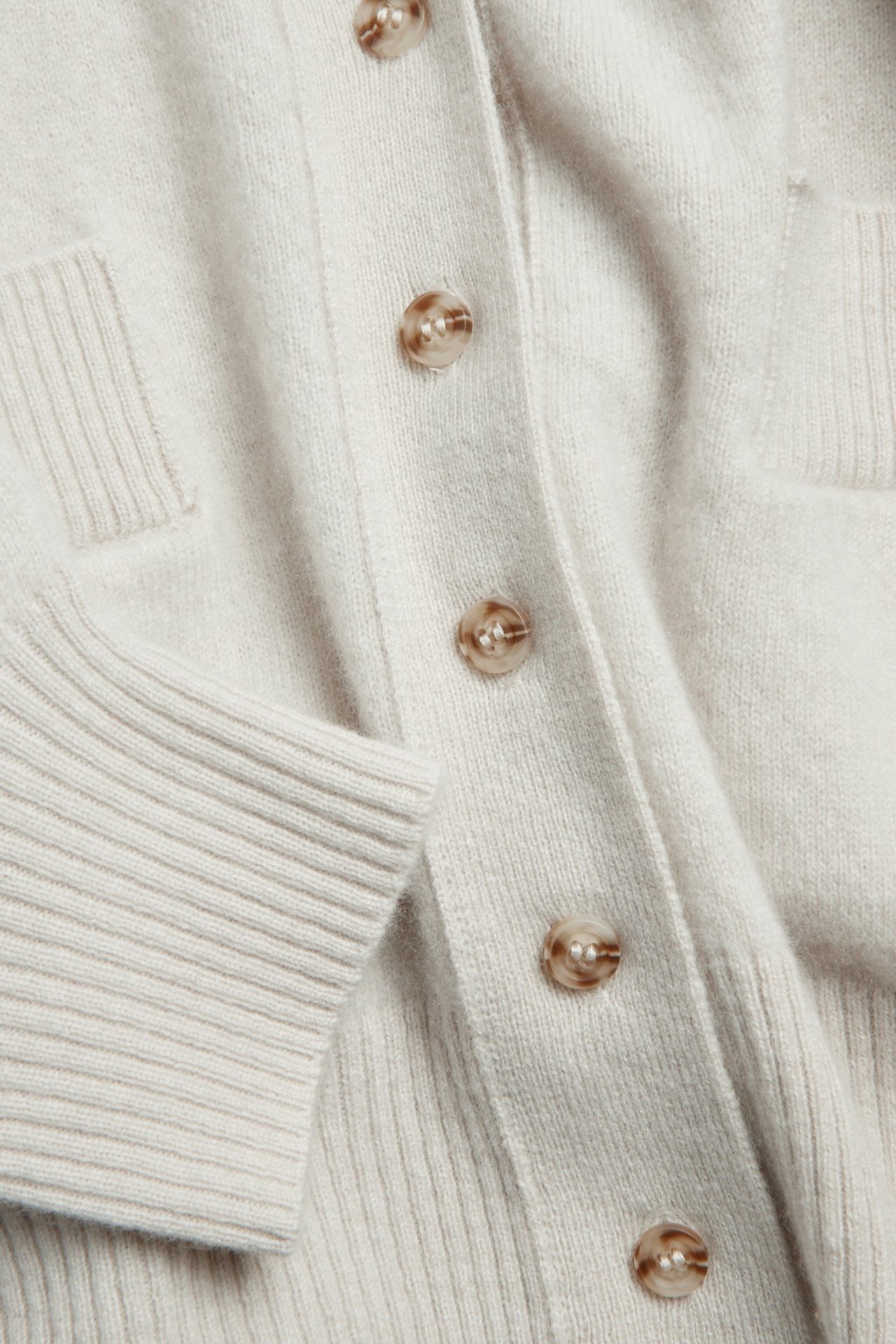 Zbliżenie na jasnobeżowy kardigan z wełny i kaszmiru z zapięciem na guziki, prążkowanym mankietem i kieszenią.