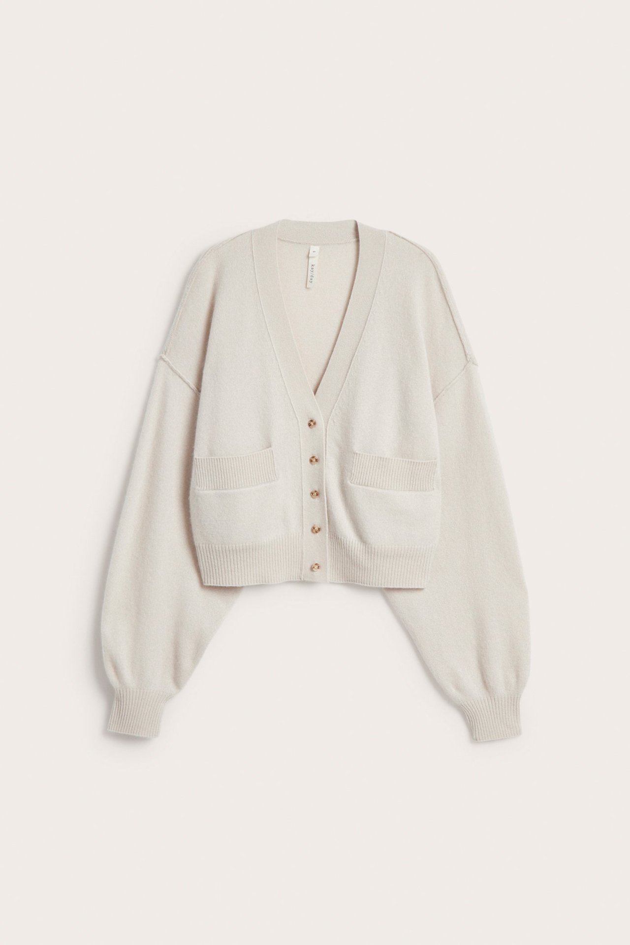 Frontbilde av en lys beige ull-kasjmir cardigan med V-hals, gullknapper og to frontlommer.