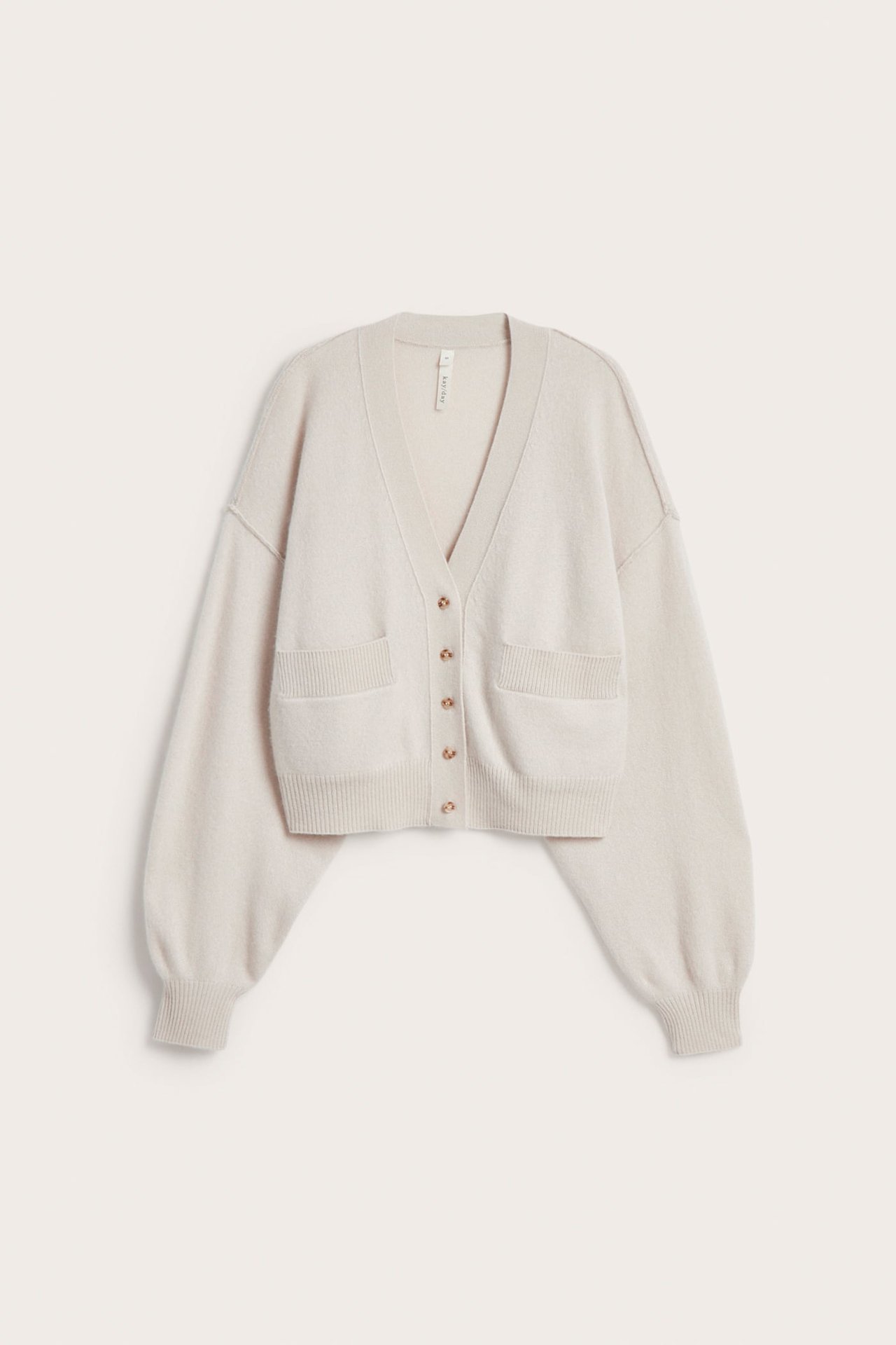 Frontbilde av en lys beige kort V-hals cardigan med seks knapper og to lommer.