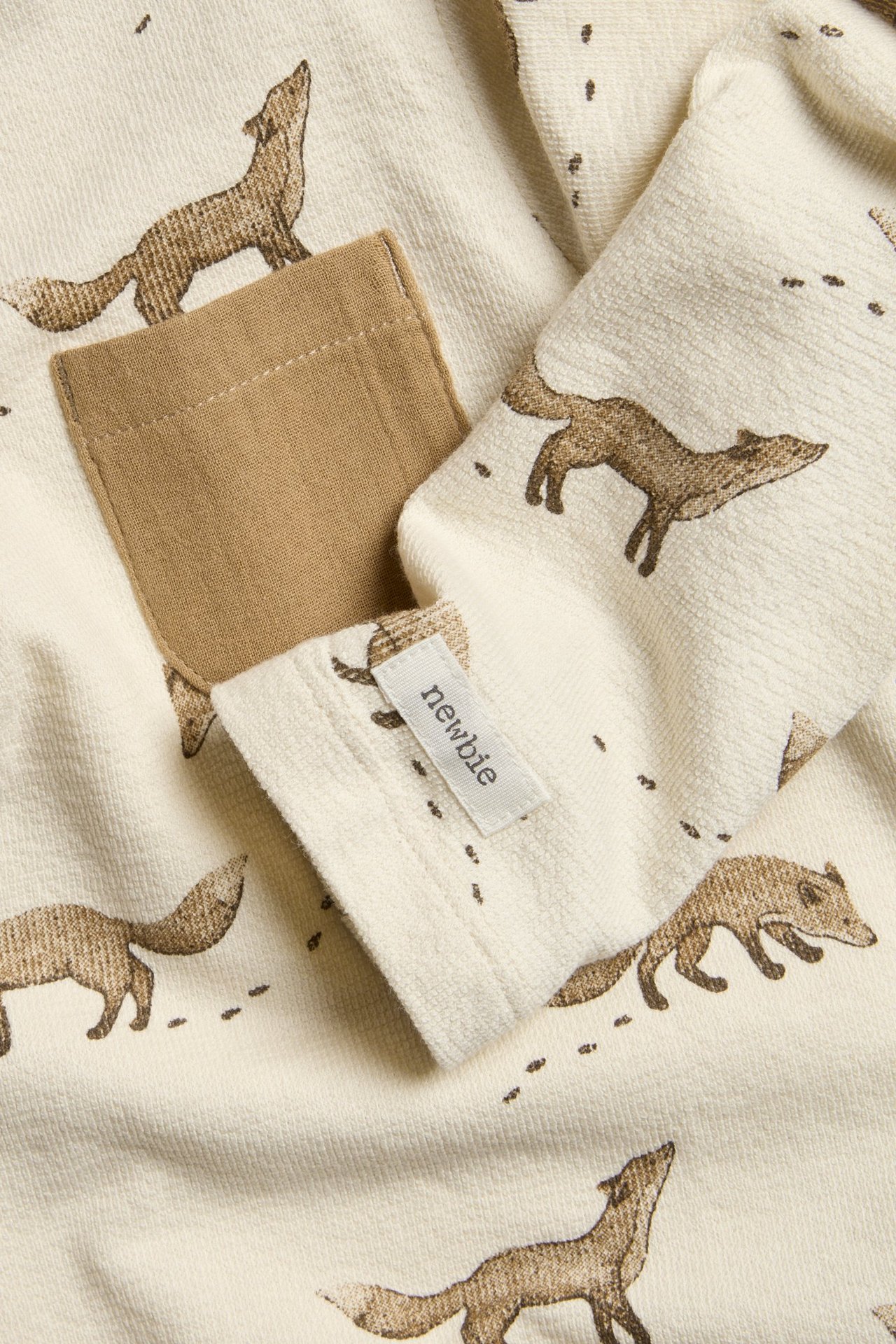 Nærbilde av en lys beige strukturert jerseytop med brunt revemønster og en lys brun brystlomme.