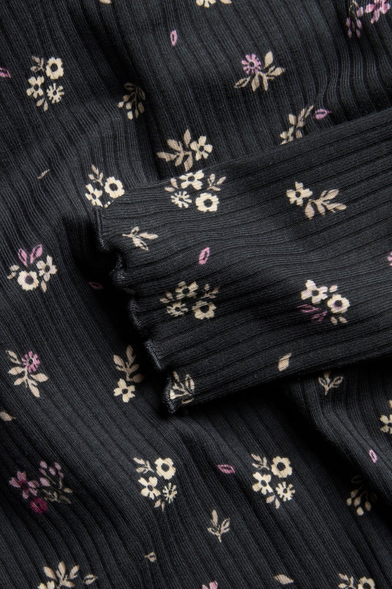 Zbliżenie czarnego prążkowanego topu z długim rękawem w beżowo-fioletowy wzór kwiatowy.