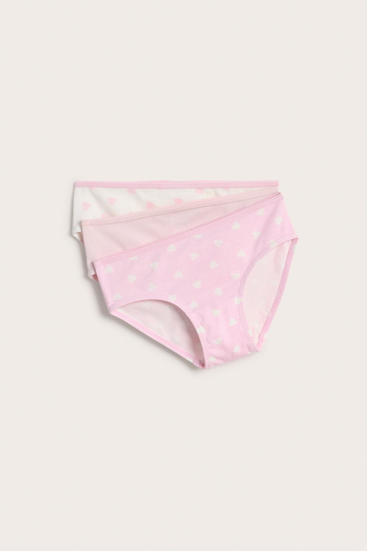Widok z góry na trzy bawełniane majtki dziecięce: dwa w serca (róż/biel), jedne gładkie jasnoróżowe.