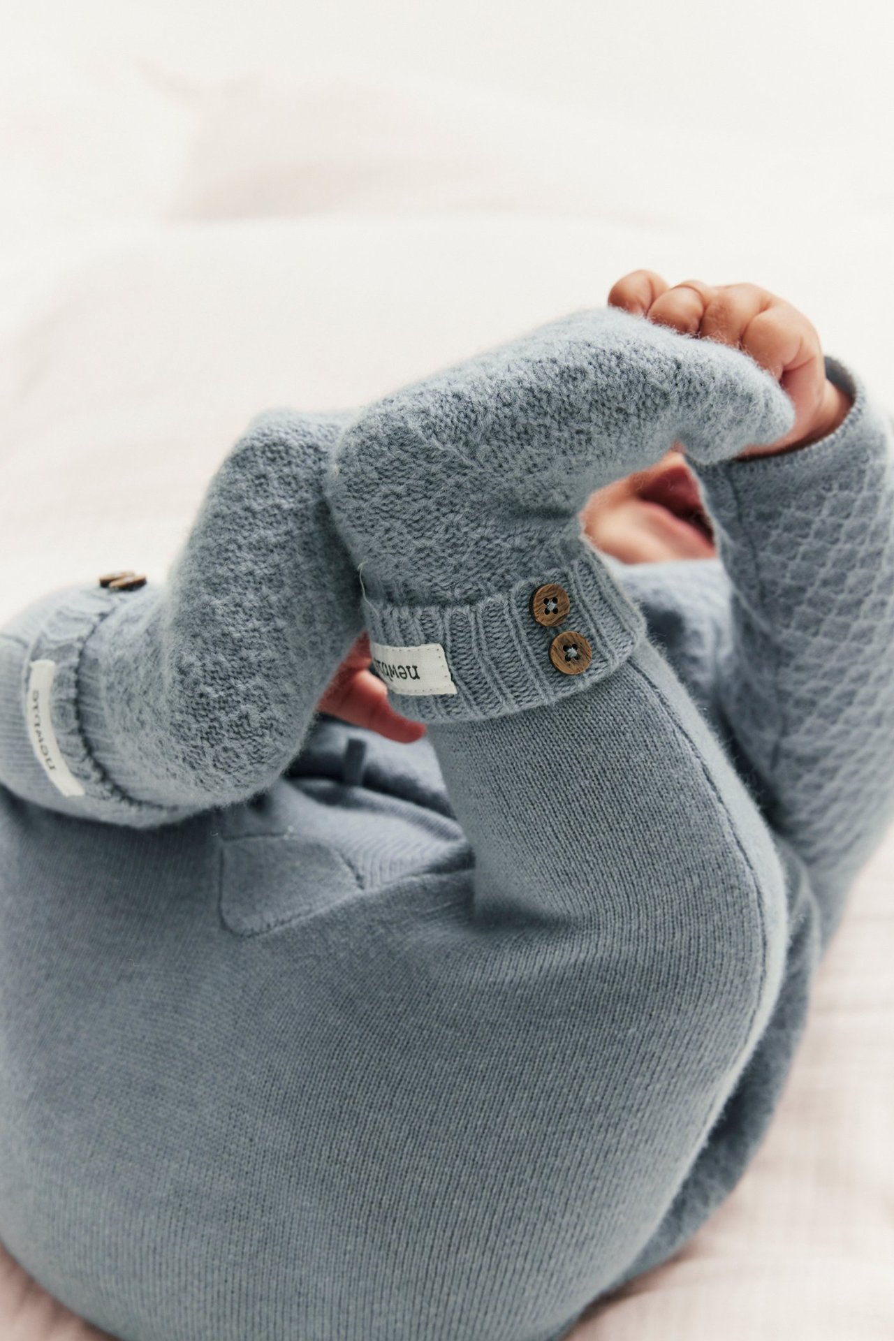 Nærbilde av baby i lyseblå strikkede ull-kasjmirbukser og matchende teksturert topp med knapper.