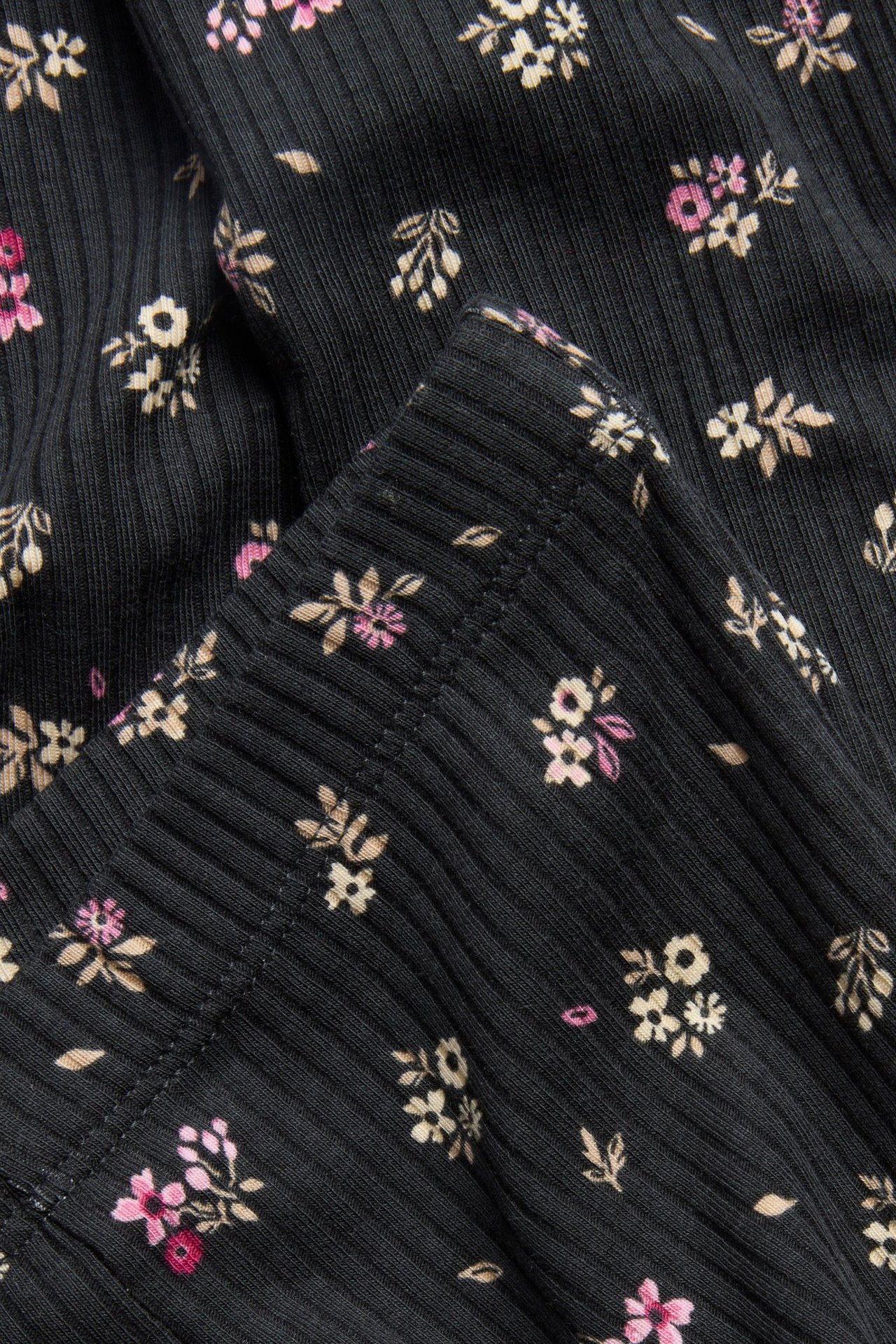 Zbliżenie czarnych prążkowanych legginsów flare z drobnym kwiatowym wzorem w różu i beżu.