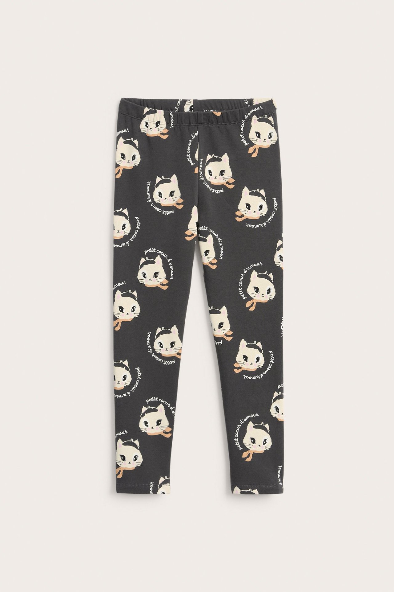 Widok z przodu na ciemnoszare wzorzyste legginsy dziecięce z białymi kocimi pyszczkami i pomarańczowymi chustami.