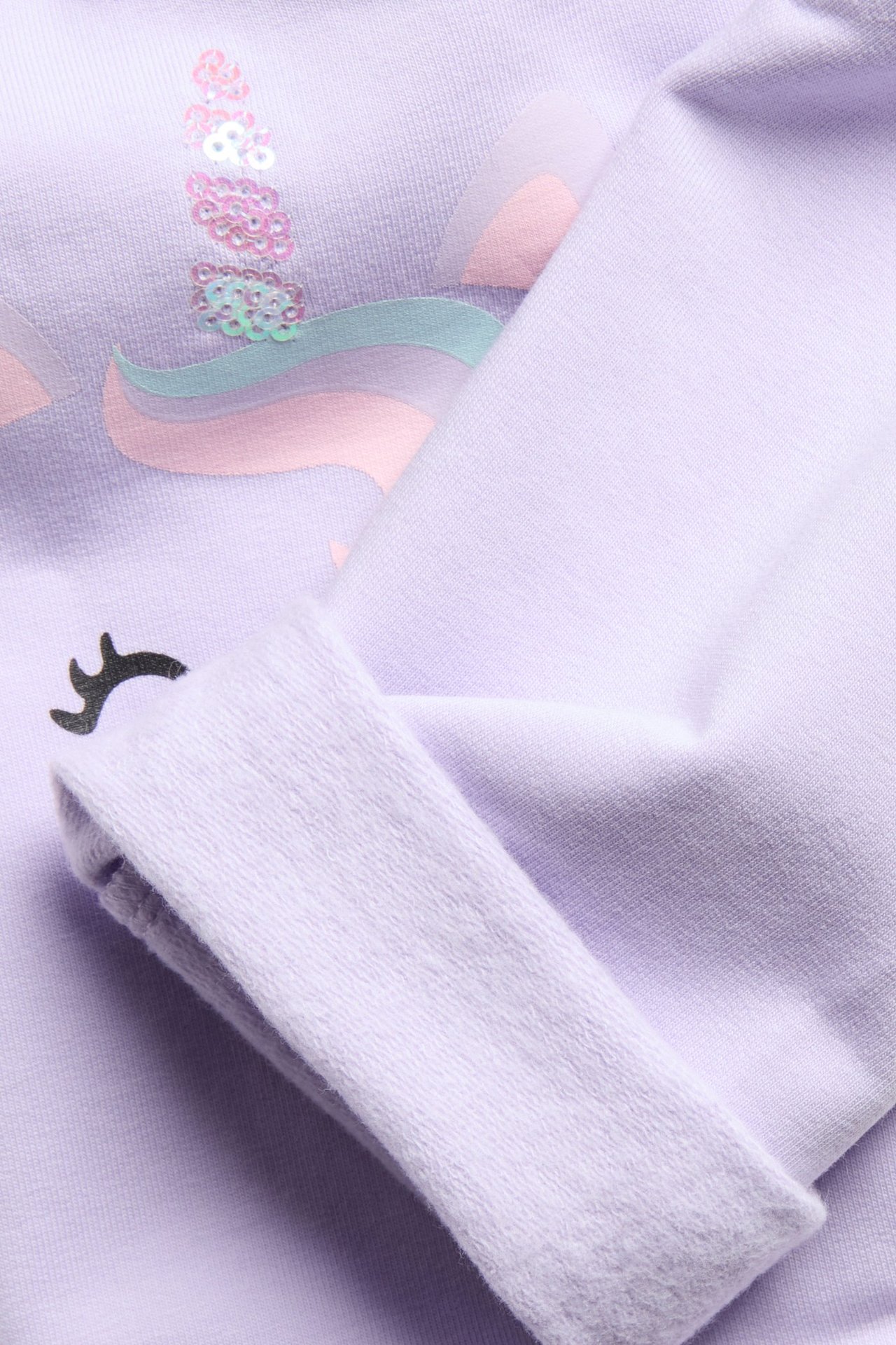 Zbliżenie na jasnofioletowe legginsy dziecięce z aplikacją jednorożca z cekinami na kolanie.