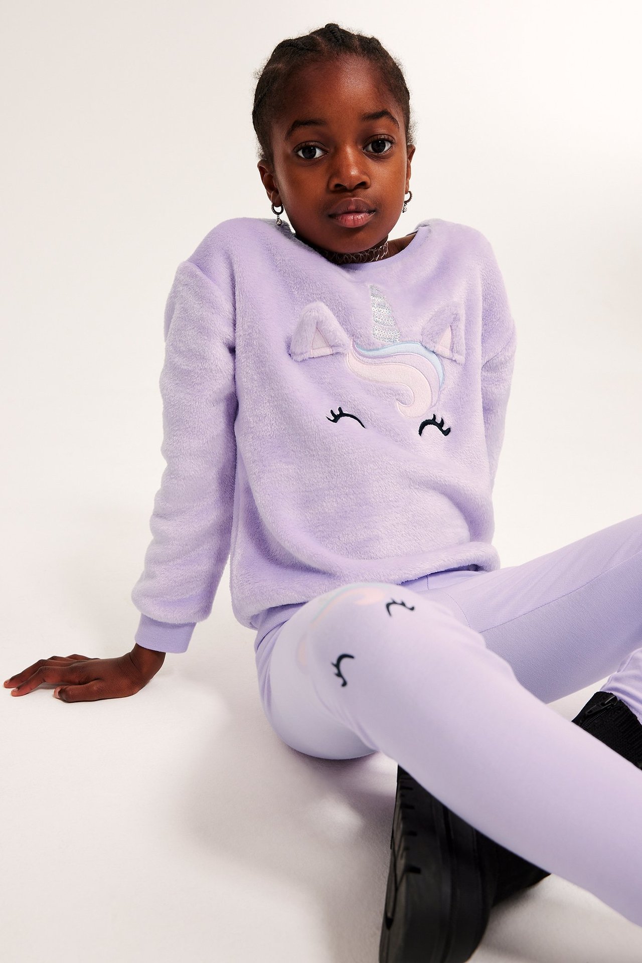 Widok z przodu dziecka w jasnofioletowych legginsach z aplikacjami jednorożca, w zestawie z puszystym swetrem.