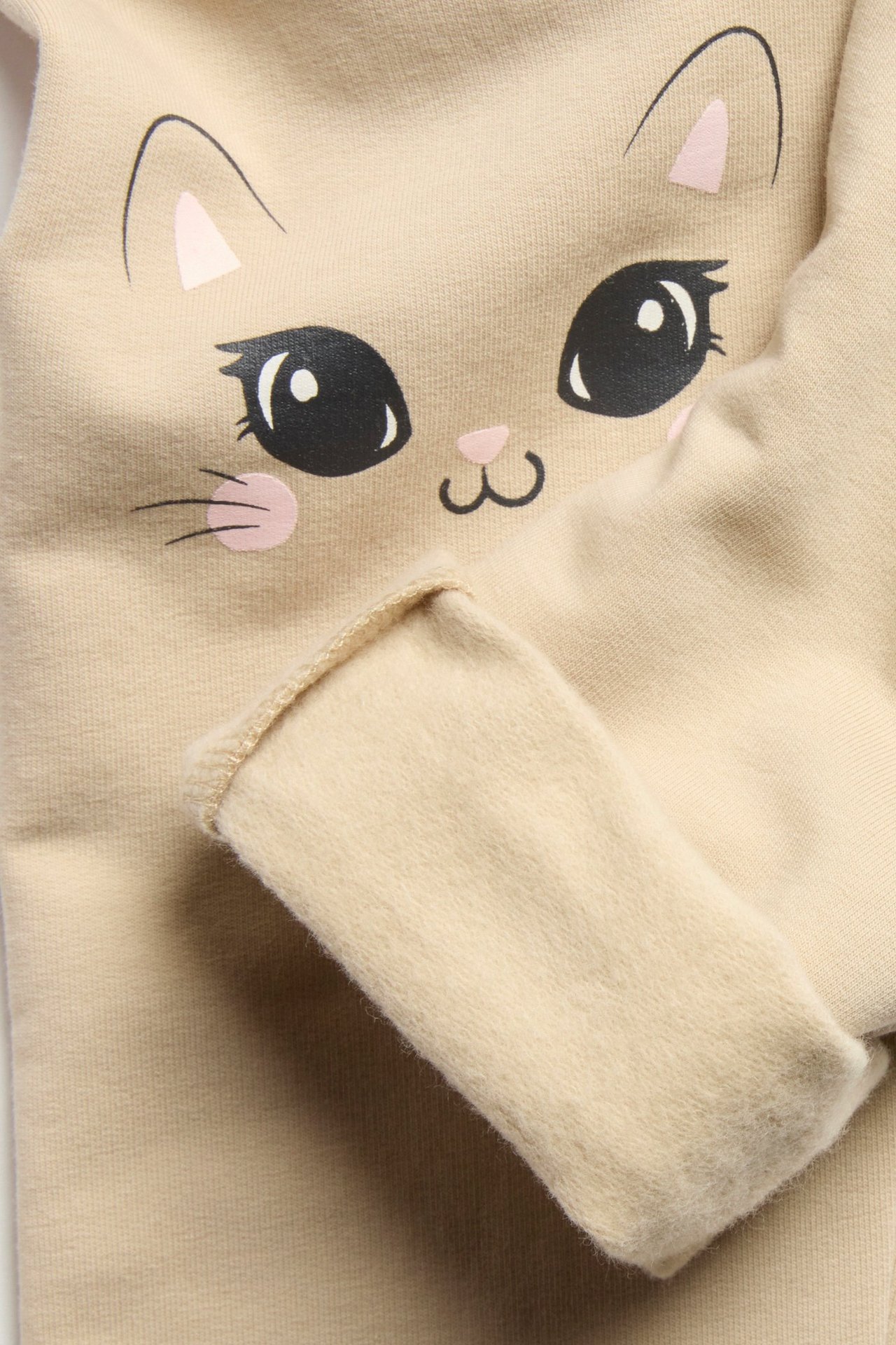 Zbliżenie na beżowe bawełniane legginsy dziecięce z czarno-różowym nadrukiem kota na kolanie.