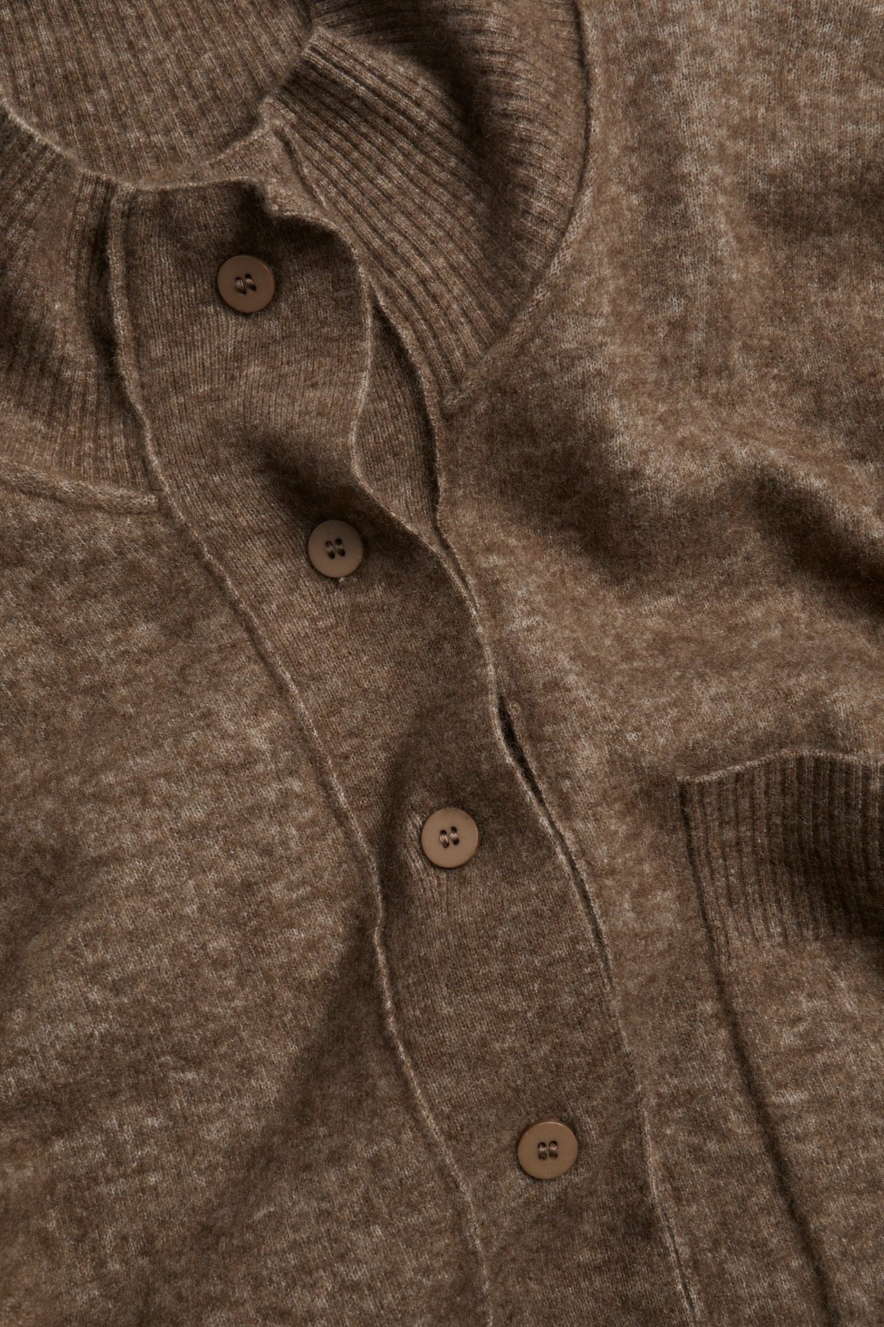 Zbliżenie brązowego melanżowego kardiganu z mieszanki wełny, z guzikami, ozdobnymi szwami i kieszenią.