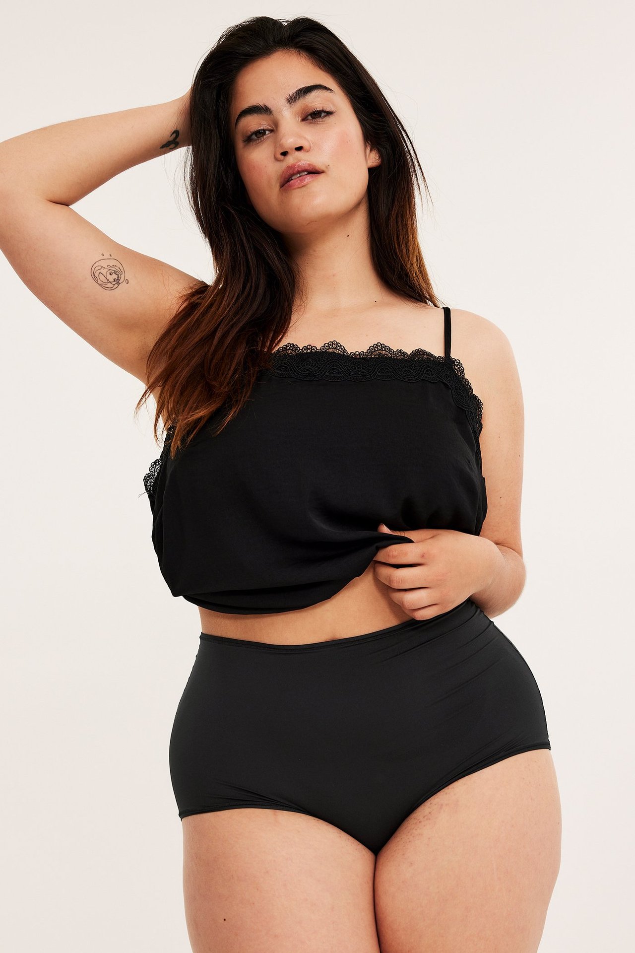 Forfra: kvinne i svarte høytlivs-hipstertruser og svart camisole med blondekant.