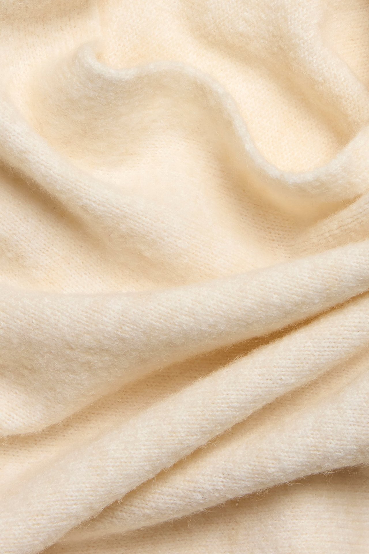 Zbliżenie miękkiego, jednolitego, kremowego dzianinowego materiału ponczo z delikatnymi fałdami.