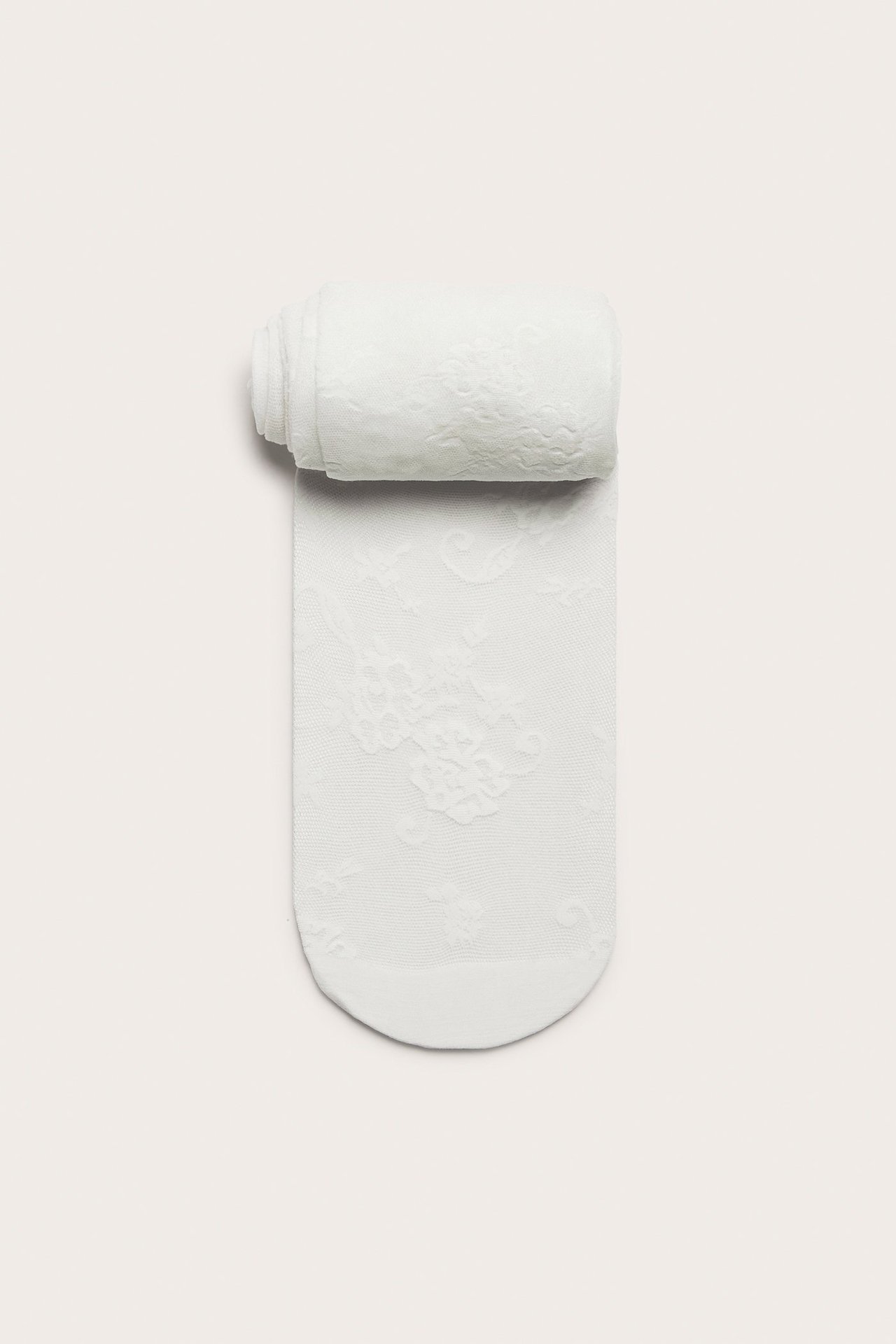 Ylhäältä kuvattu: luonnonvalkoiset pitsikuvioiset sukkahousut, rullattu ylhäältä, litteänä.