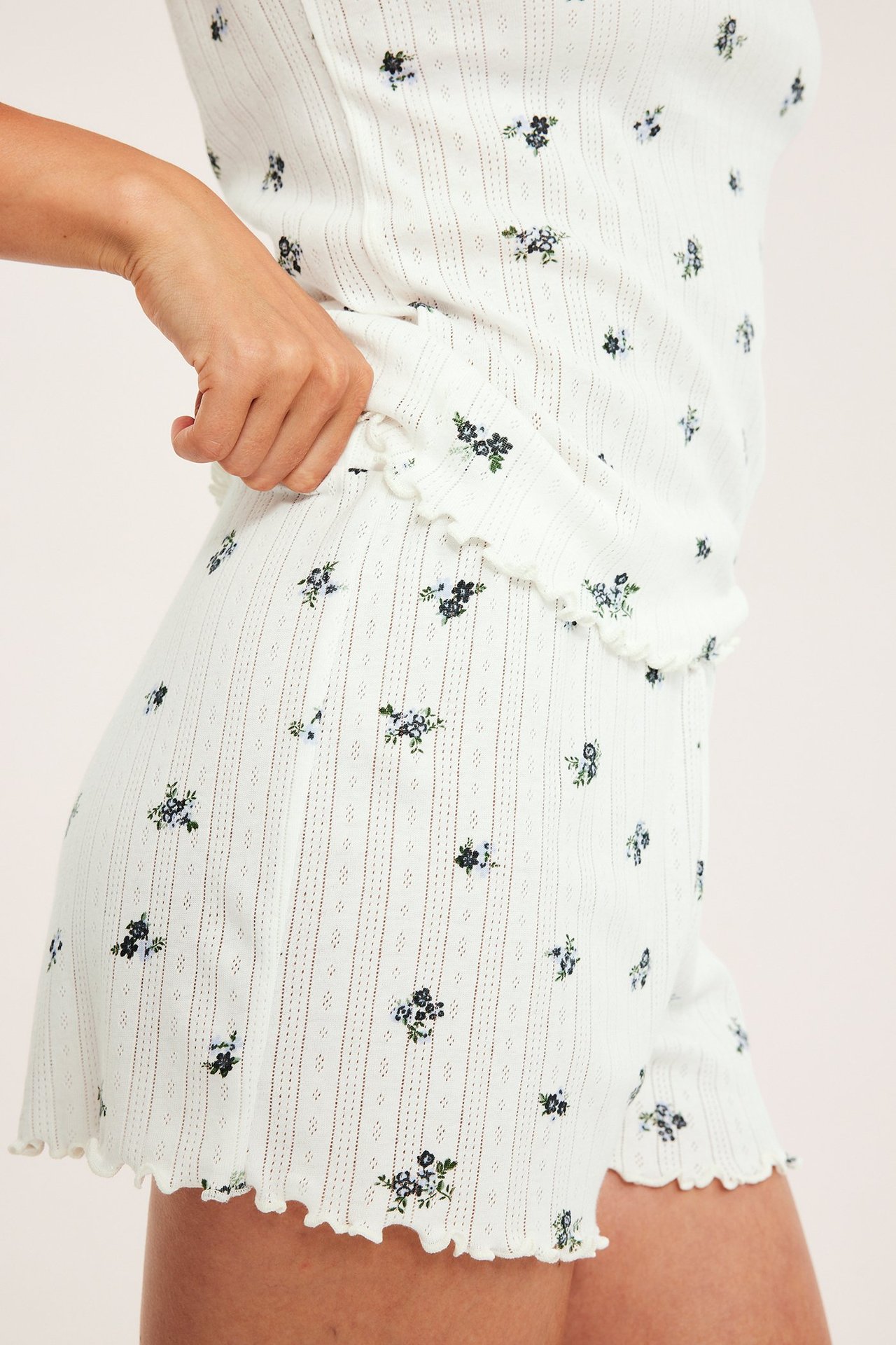 Lähikuva, sivukuva: nainen valkoisessa pointelle-pyjamasetissä, jossa tummansininen kukkakuvio, röyhelöreunat.