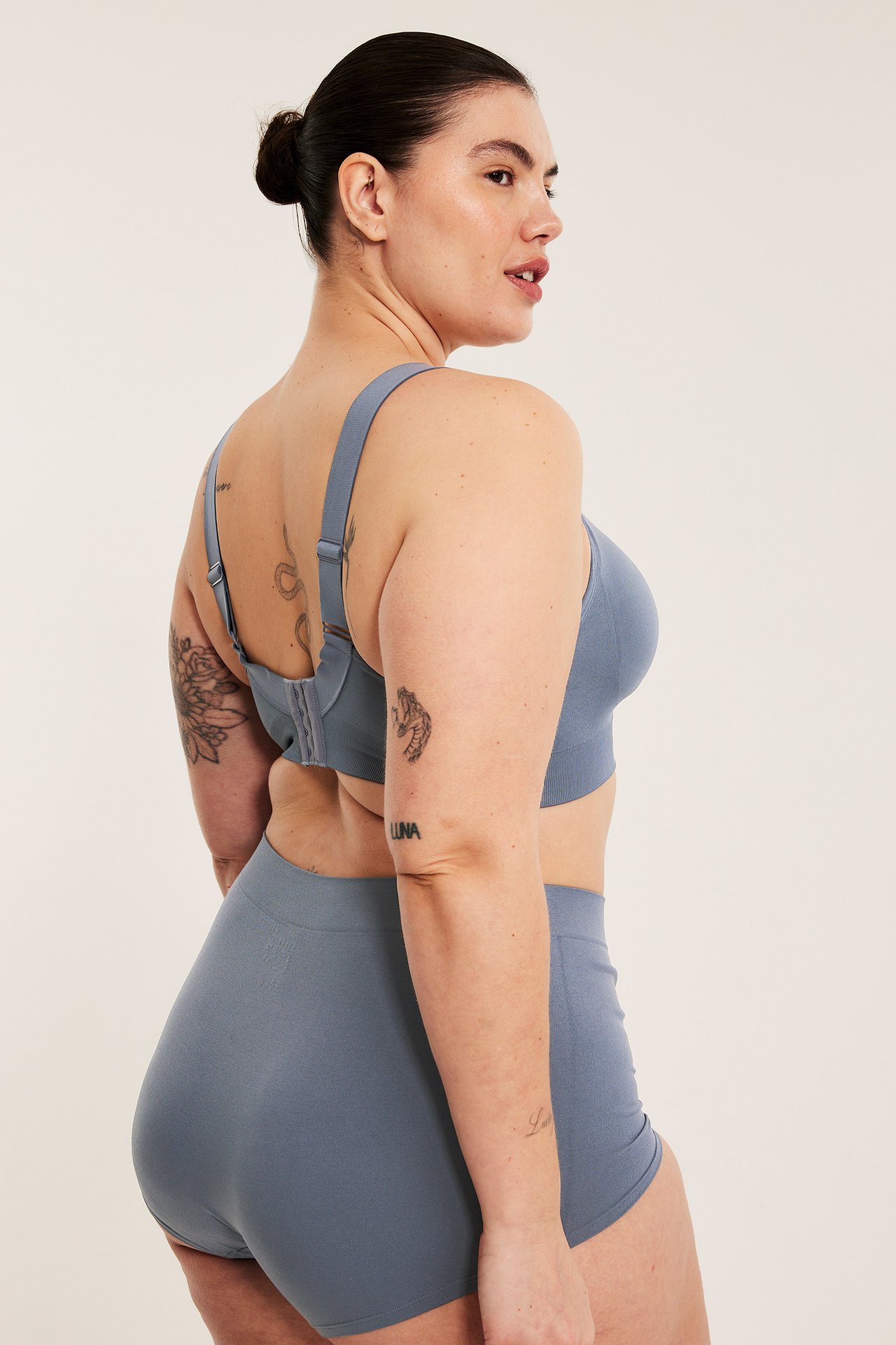 Naisen sivu-takaapäin näkymä tummansinisistä saumattomista kaarituettomista rintaliiveistä ja yhteensopivista shortseista.