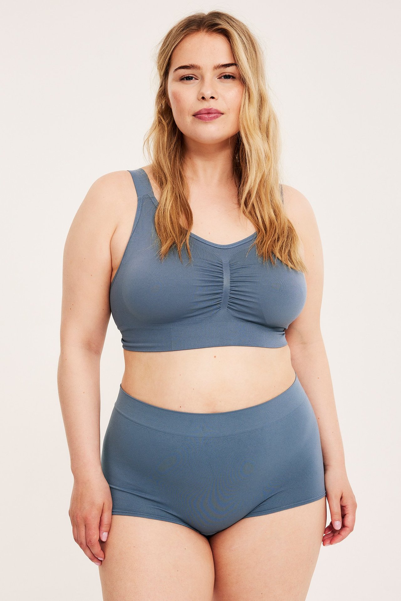 Framifrån, kvinna i mörkblå sömlös bygellös bh med rynkad front och matchande shorts.
