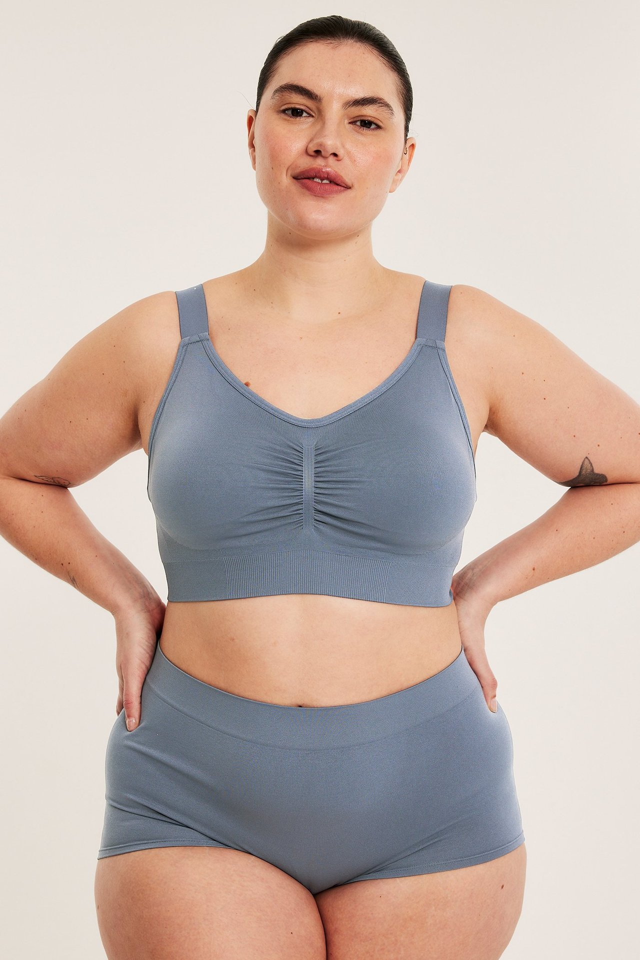 Naisen etukuva tummansinisessä saumattomassa kaarituettomassa rintaliivissä rypytyksellä ja yhteensopivissa saumattomissa shortseissa.