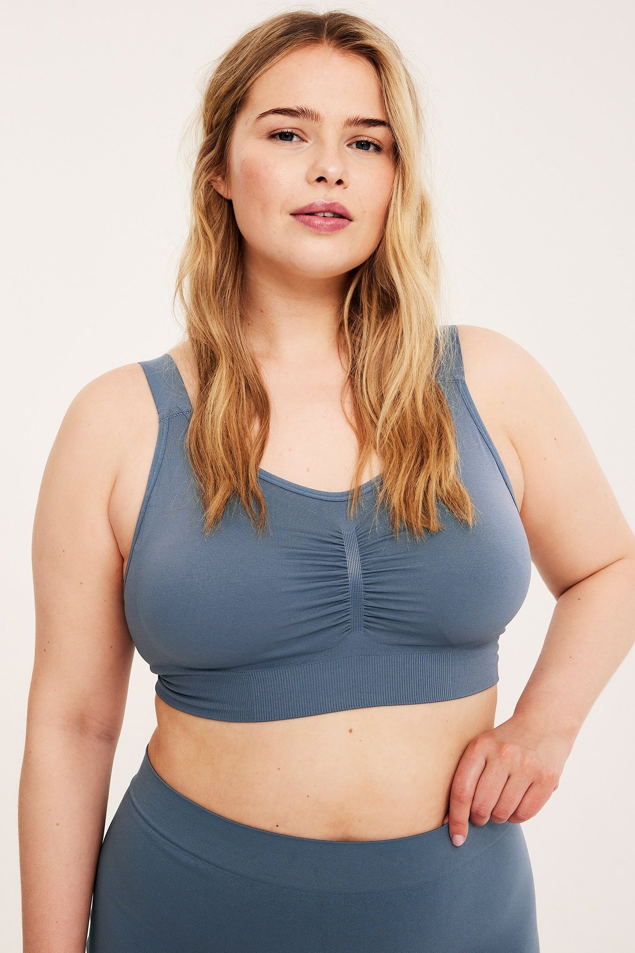 Edestä, nainen yllään tummansininen saumaton kaaritueton rintaliivi rypytyksellä ja yhteensopivat alaosat.