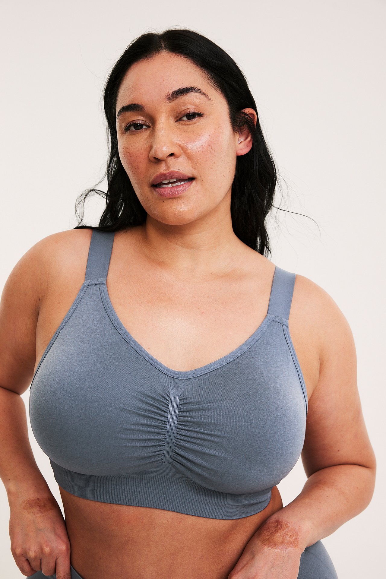 Framifrån, en kvinna i en mörkblå sömlös bygellös bh med rynkad front och matchande underdel.