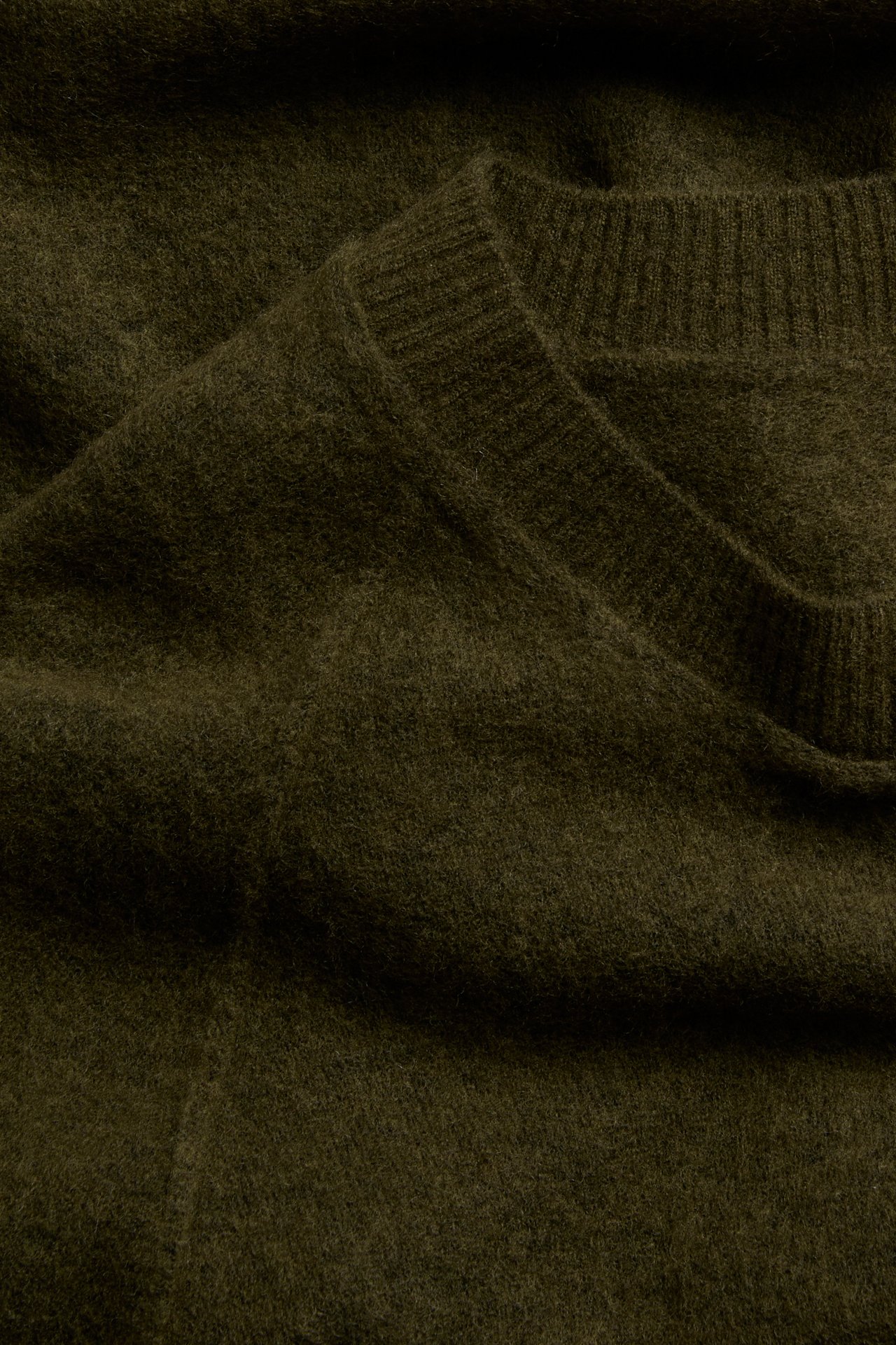 Zbliżenie oliwkowozielonego, włochatego swetra z dzianiny, ze ściągaczem przy dekolcie.