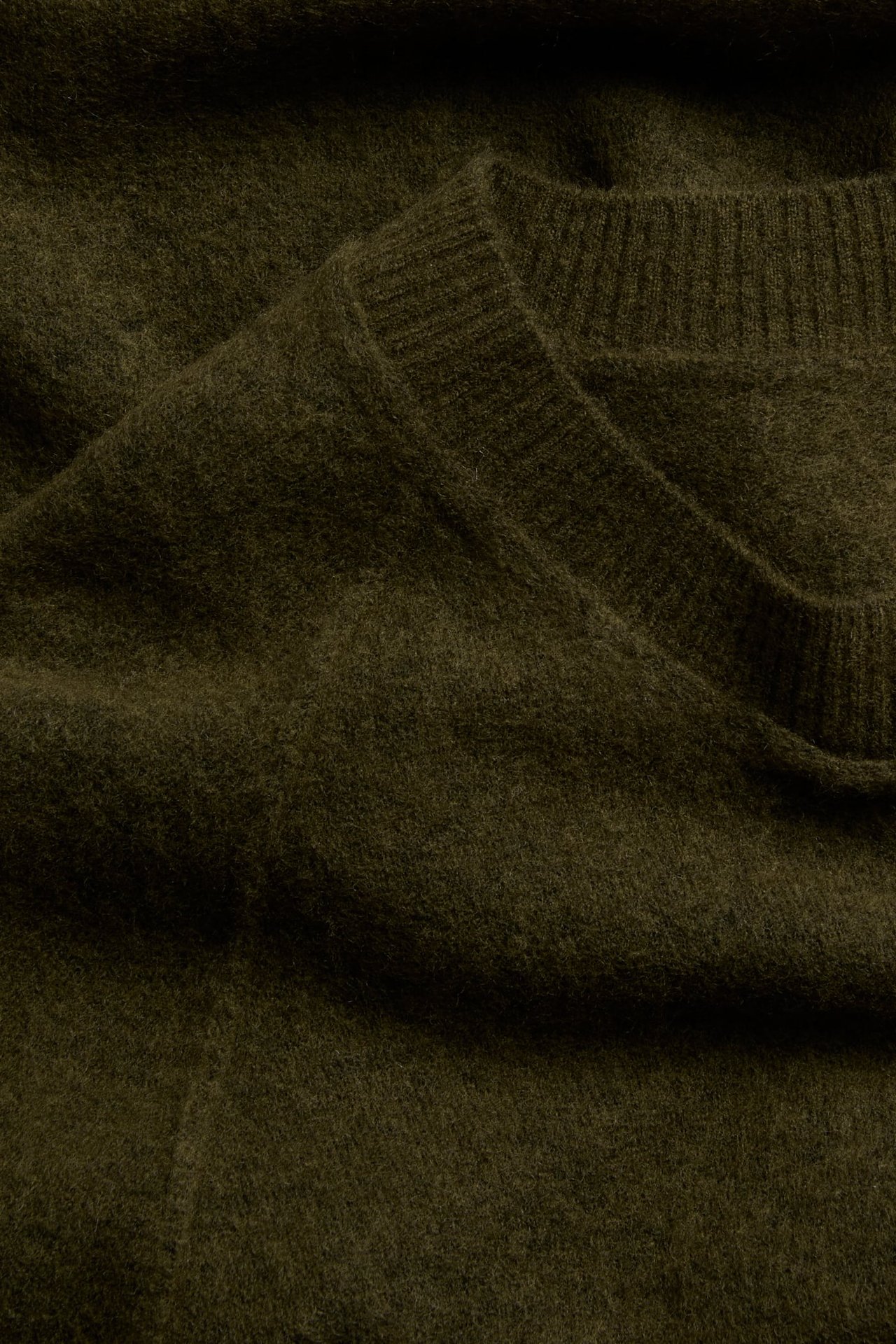 Zbliżenie oliwkowozielonego, włochatego swetra z dzianiny, ze ściągaczem przy dekolcie.