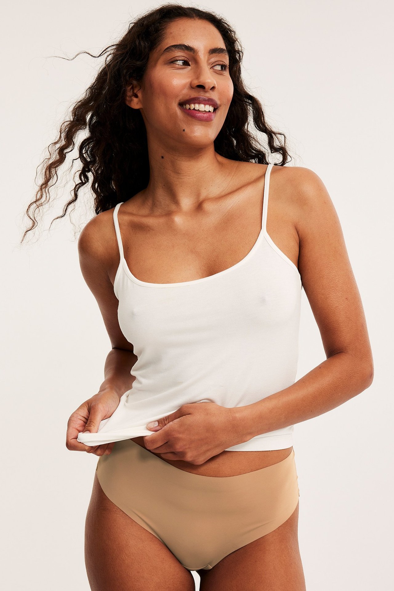 Edestäpäin, nainen yllään ruskeat saumattomat stringit ja valkoinen spagettiolkaiminen toppi.