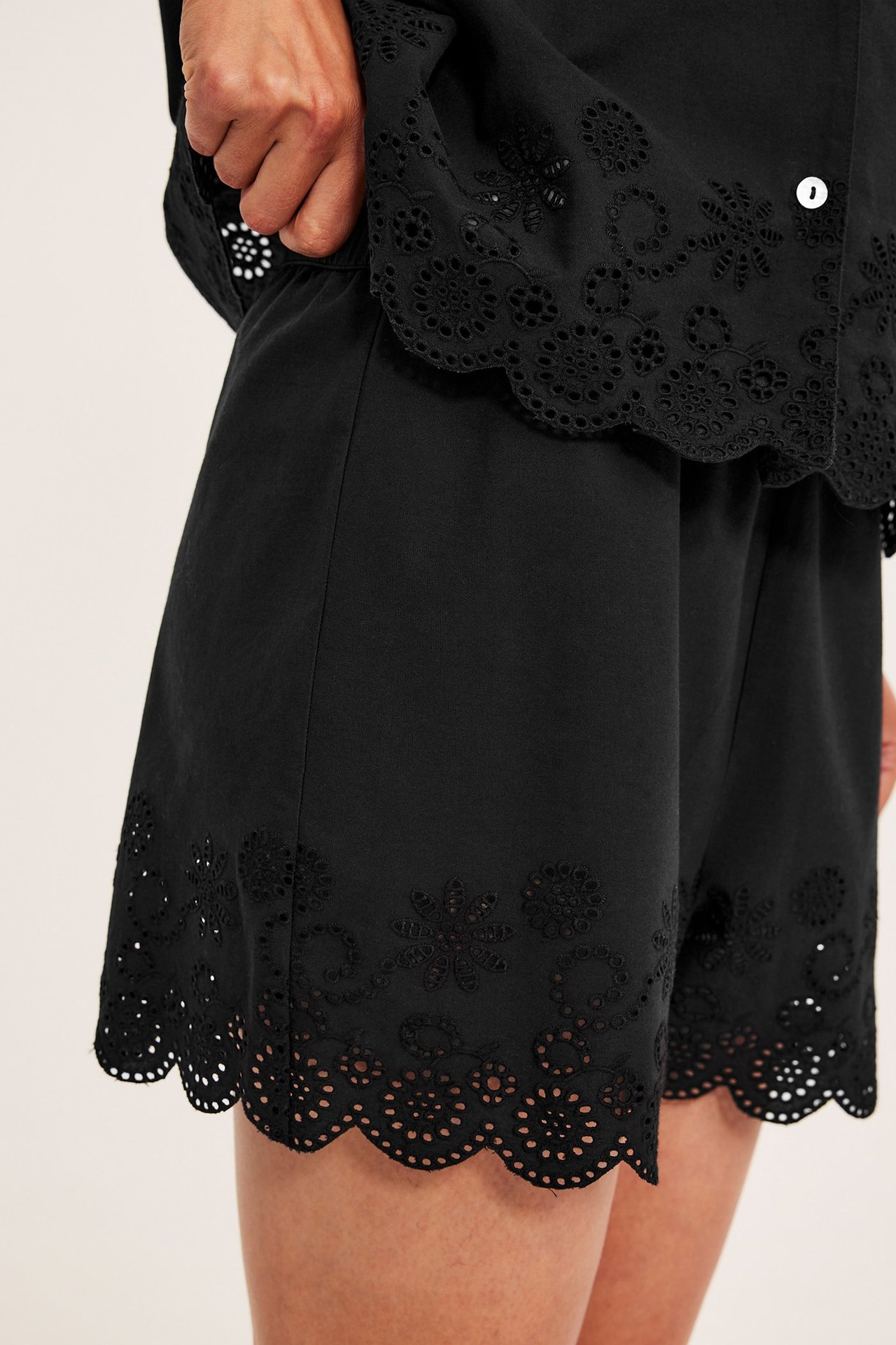 Lähikuva edestä: Nainen mustissa puuvillapyjamashortseissa brodeeratulla aaltoreunalla ja yhteensopivalla topilla.