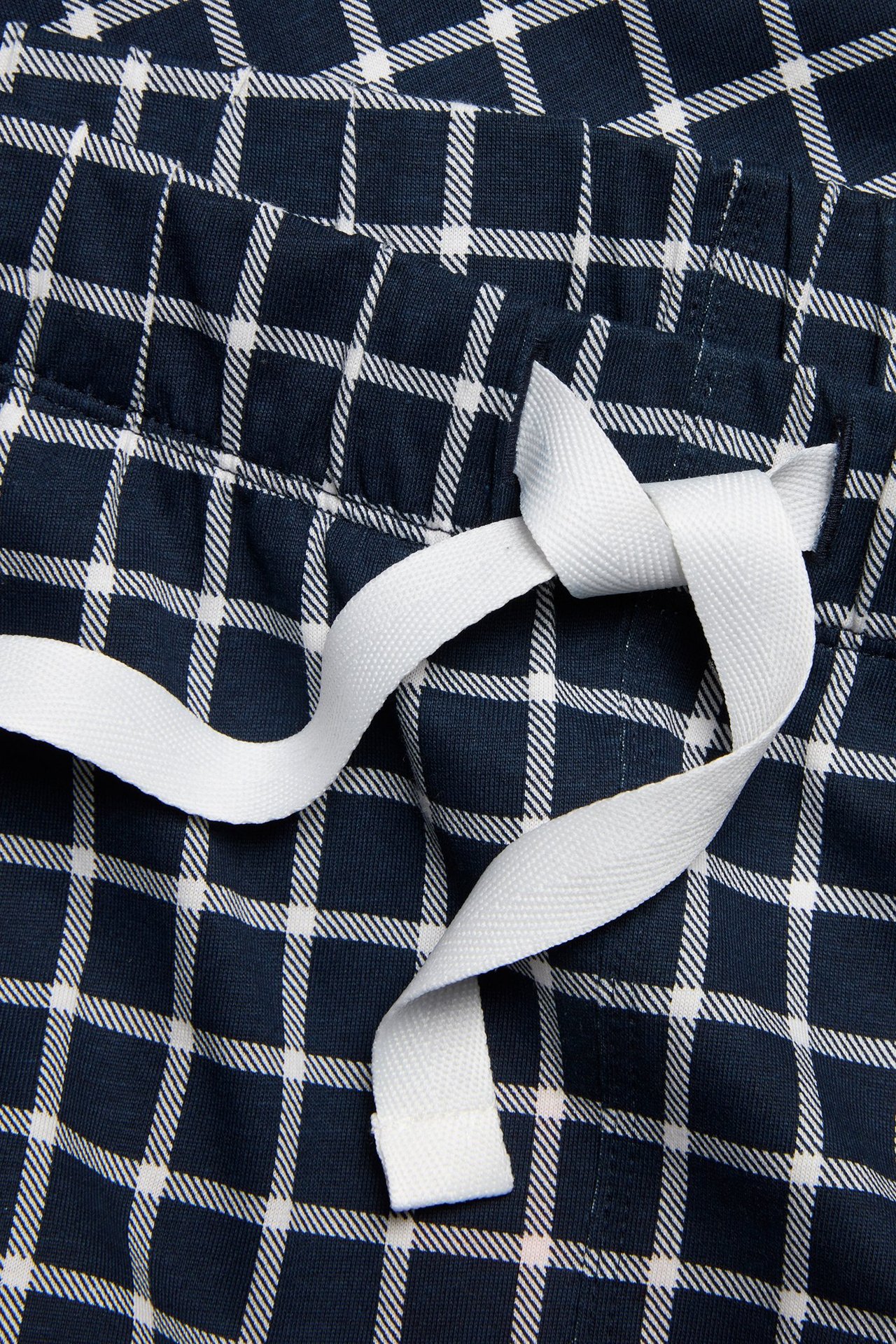 Zbliżenie na granatowe bawełniane spodnie piżamowe w kratę z białym sznurkiem w pasie.