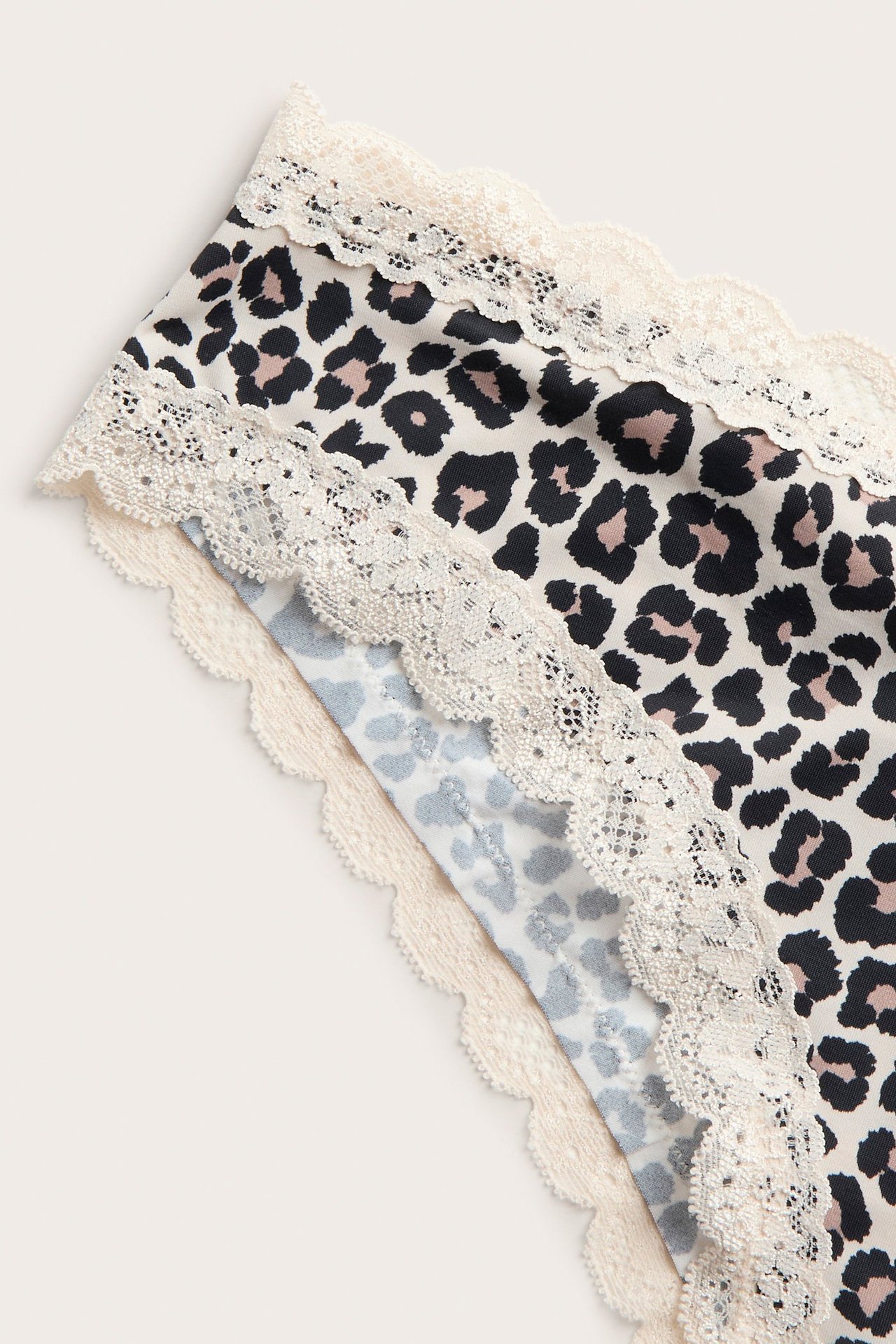Zbliżenie na trzy ułożone w stos damskie figi cheeky: beżowe w panterkę, jasnoniebieskie i jednolicie beżowe, wszystkie z koronkową lamówką.