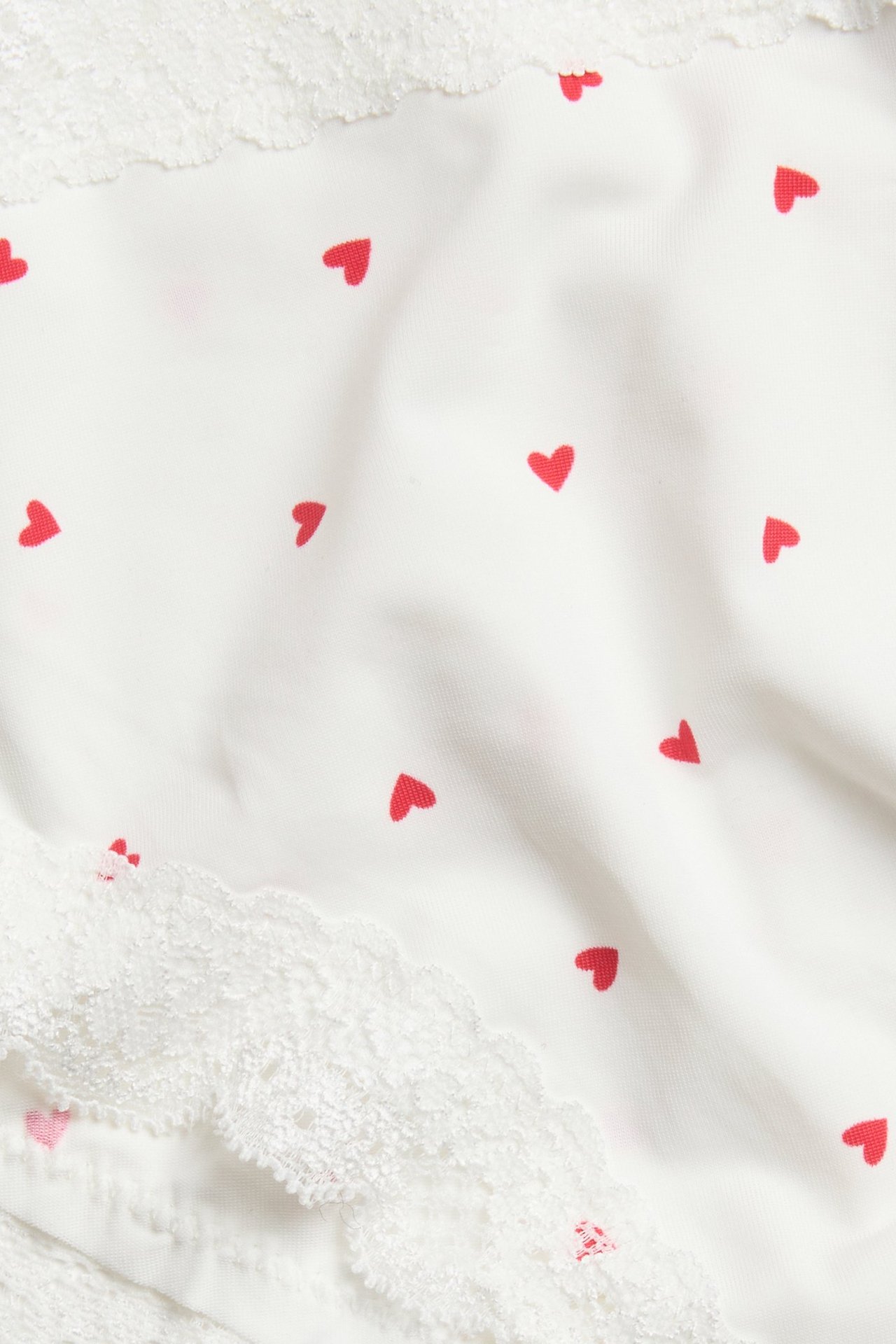 Zbliżenie na off-white damskie figi cheeky z czerwonym wzorem serc i białą koronką.