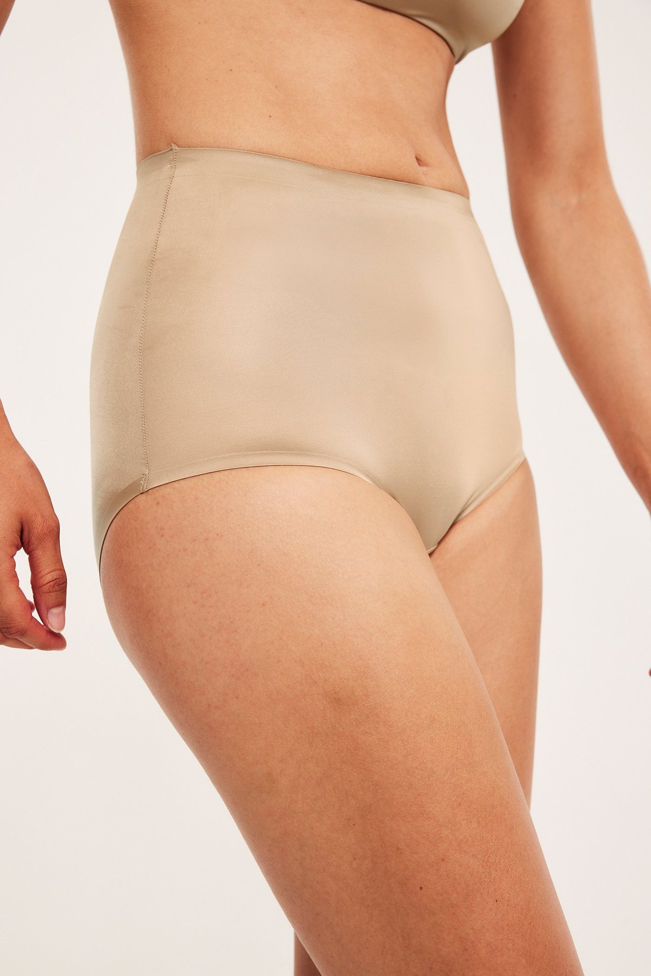 Sidovy av kvinna i högmidjade beiga shapingtrosor av slät, sömlös satinmicro.