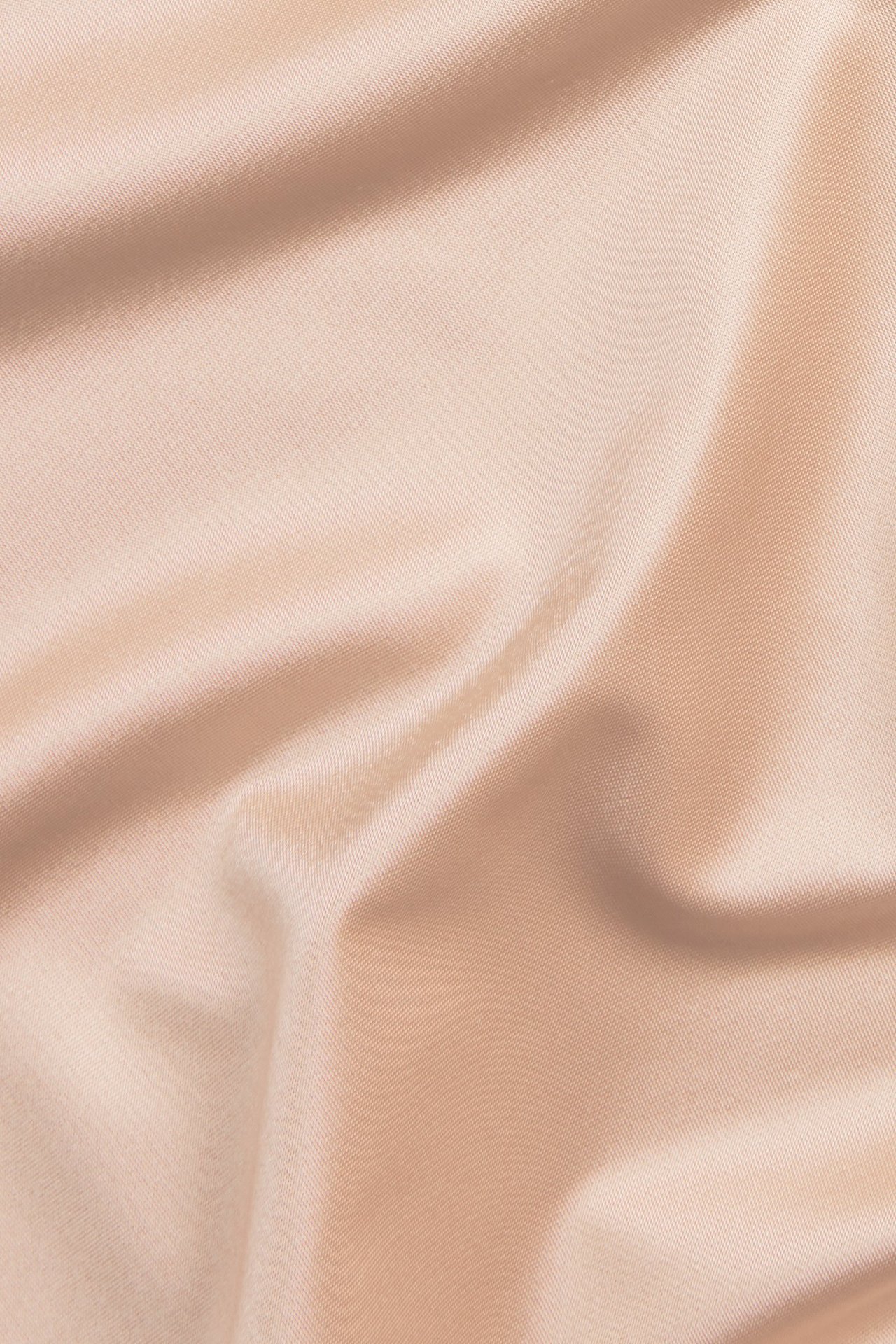 Zbliżenie jasnoróżowej tkaniny satynowej z mikrofibry z miękkimi, gładkimi fałdami.