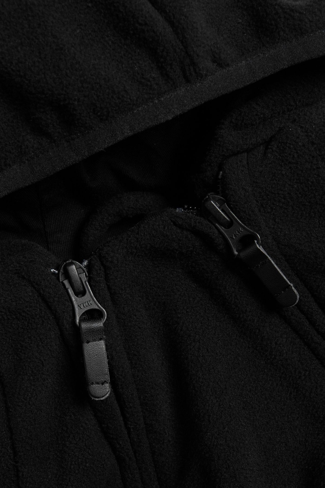 Zbliżenie czarnego polarowego kombinezonu dla niemowląt, pokazujące zamek błyskawiczny i kaptur.