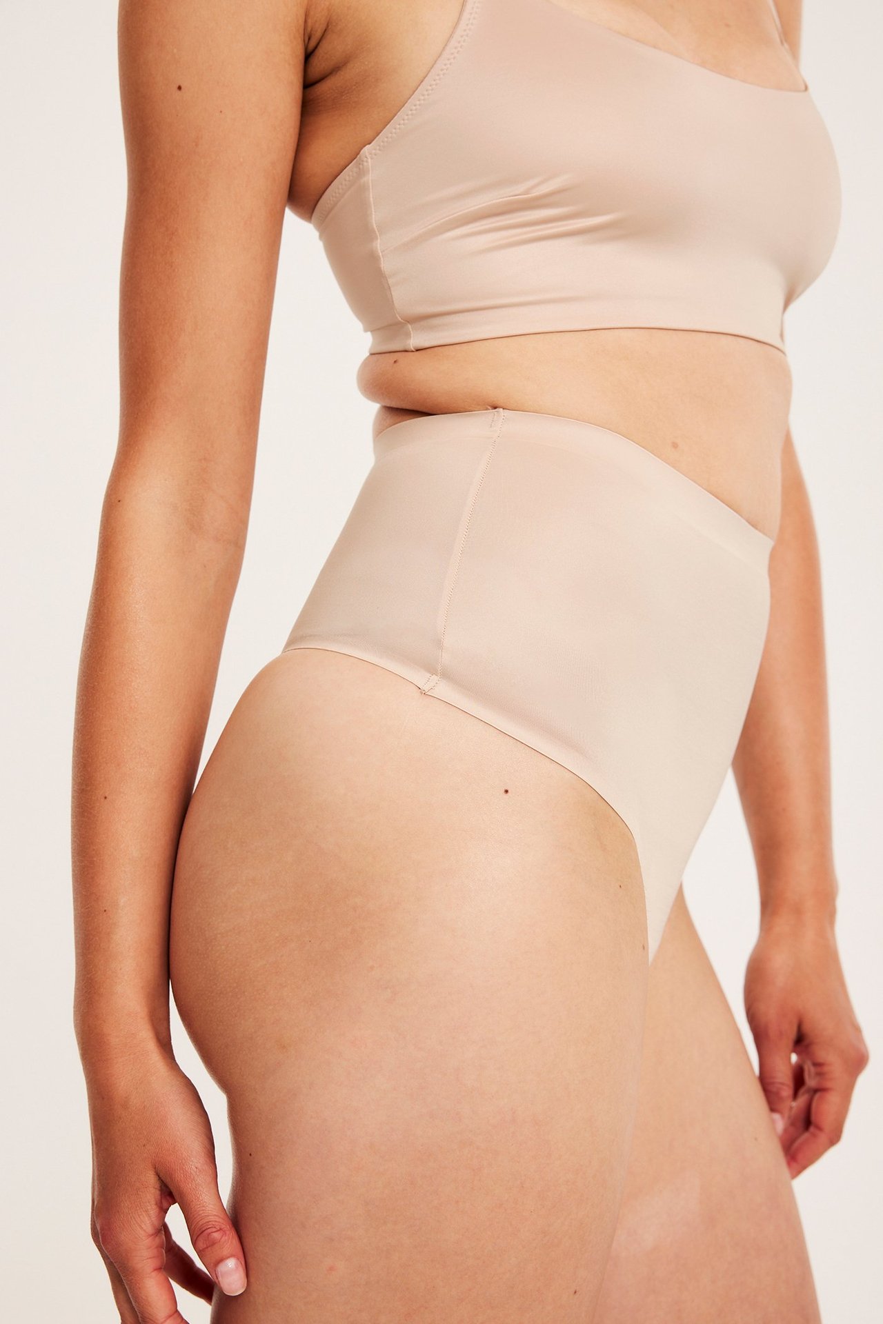 Sidebilde av kvinne i lys rosa høy midje satinmicro shaping-stringtruse og matchende BH-topp.