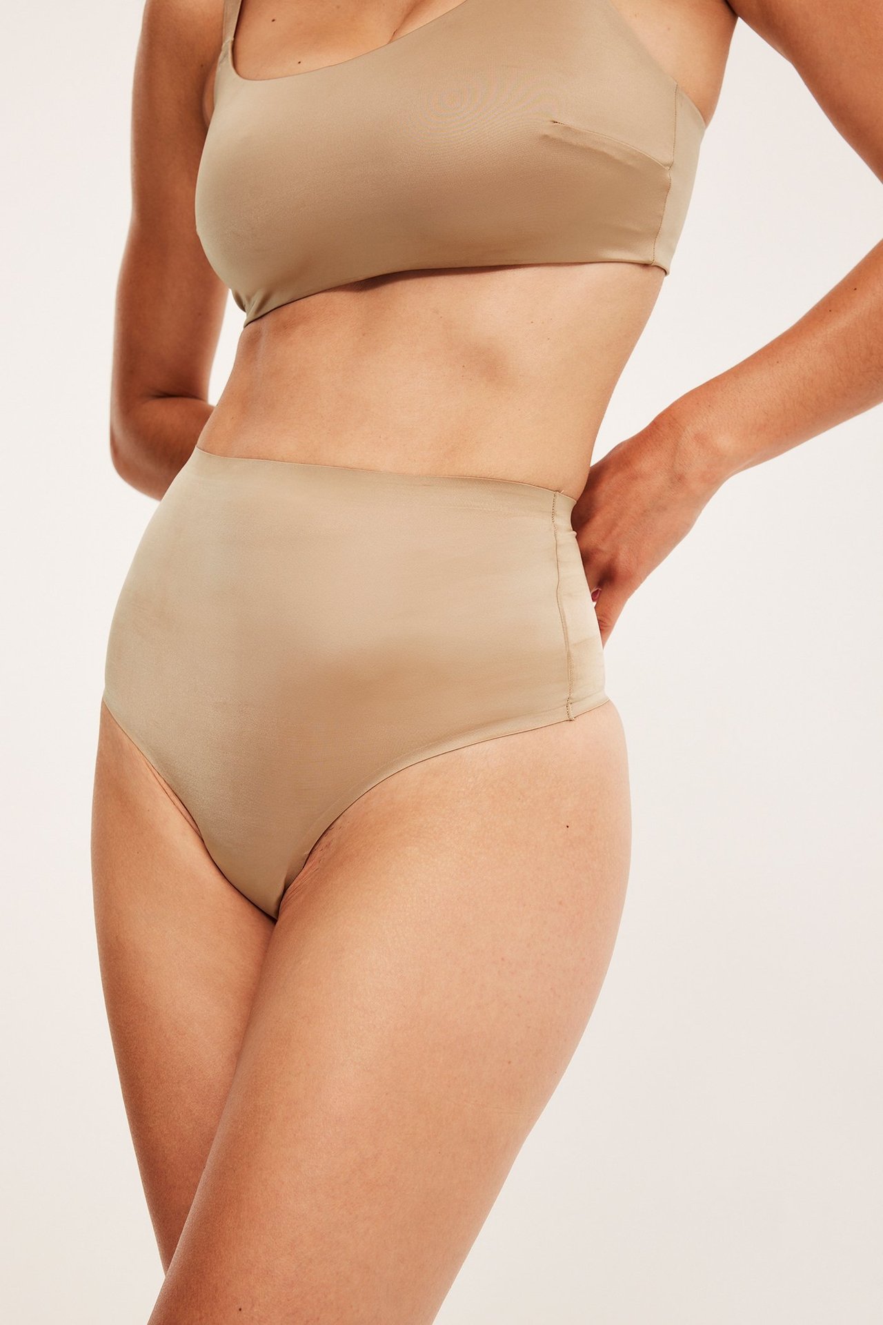 Framifrån: kvinna i högmidjad brun shapingstringtrosa och matchande brun BH.