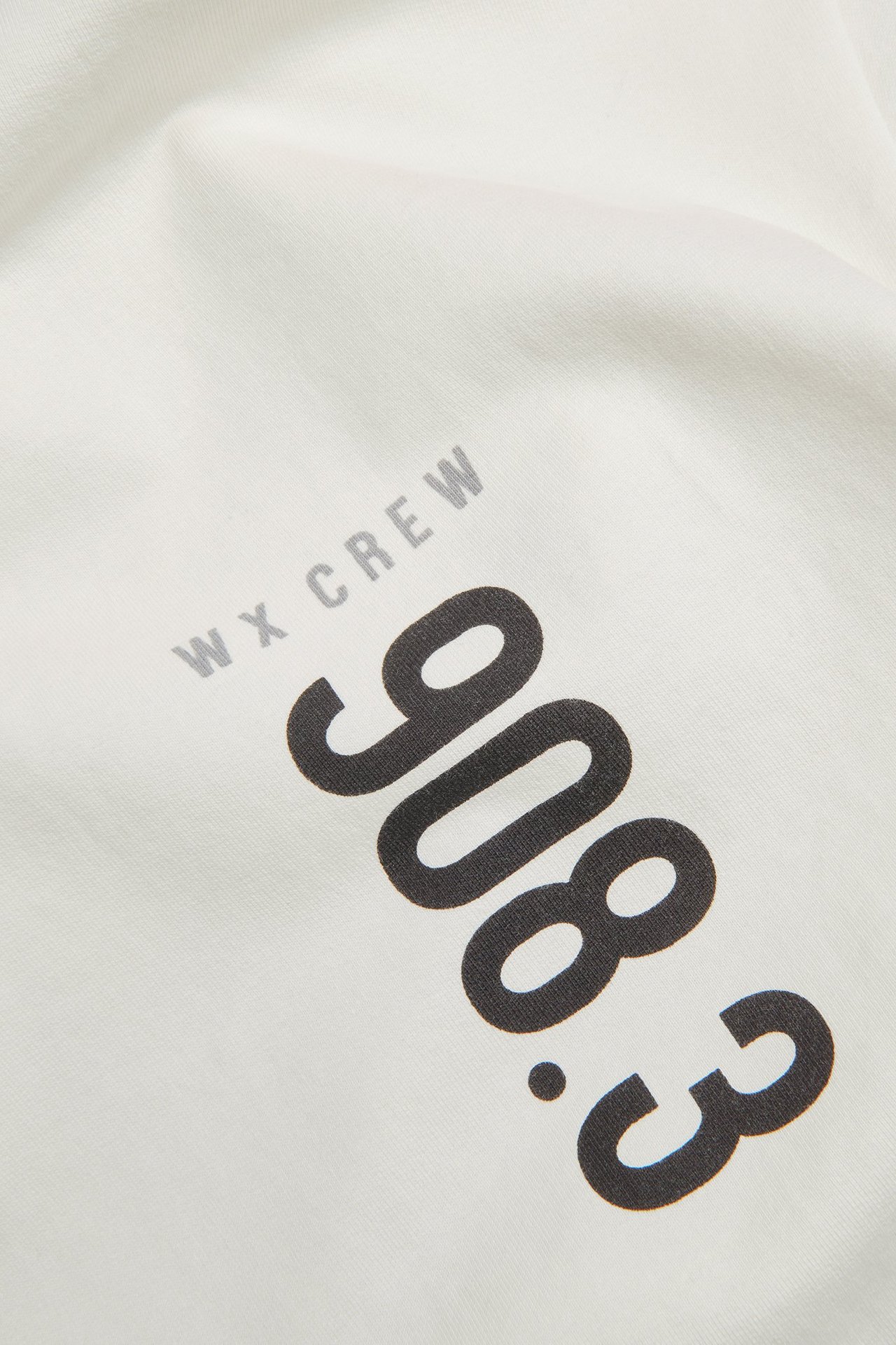 Zbliżenie na białą bawełnianą koszulkę z czarnym nadrukiem '908.3' i szarym 'WX CREW'.