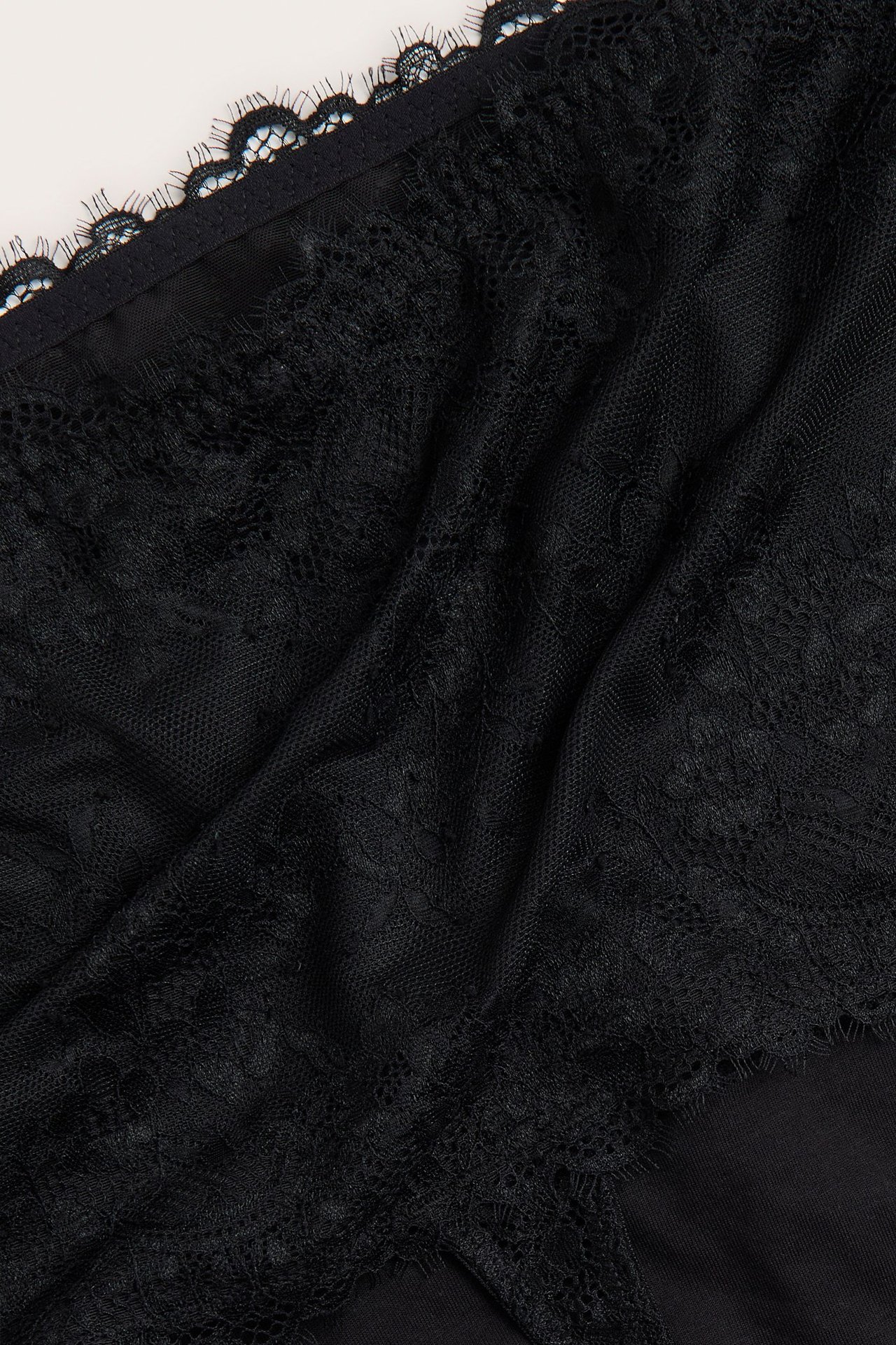 Zbliżenie na czarne koronkowe stringi z wysokim stanem i podszewką power mesh.